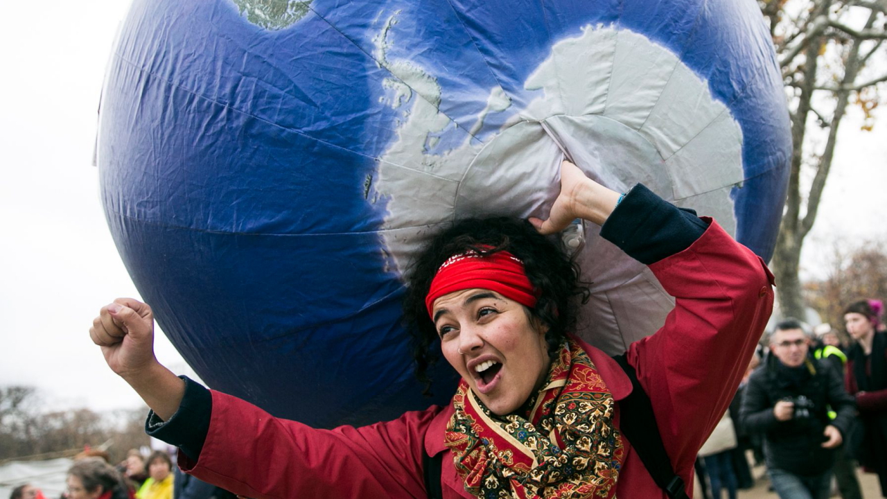 Eine Demonstrantin mit einem aufblasbaren Globus auf der Schulter bei der Demo anlässlich der Klimakonferenz von Paris (Archivbild von 2015). | ETIENNE LAURENT/EPA-EFE/Shutters