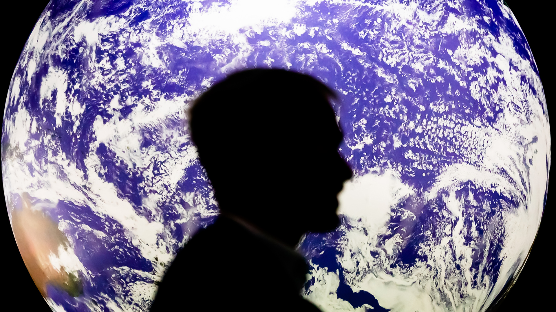 Ein Mann sitzt bei der UN-Klimakonferenz in Glasgow vor einem leuchtenden Globus. | Bildquelle: dpa