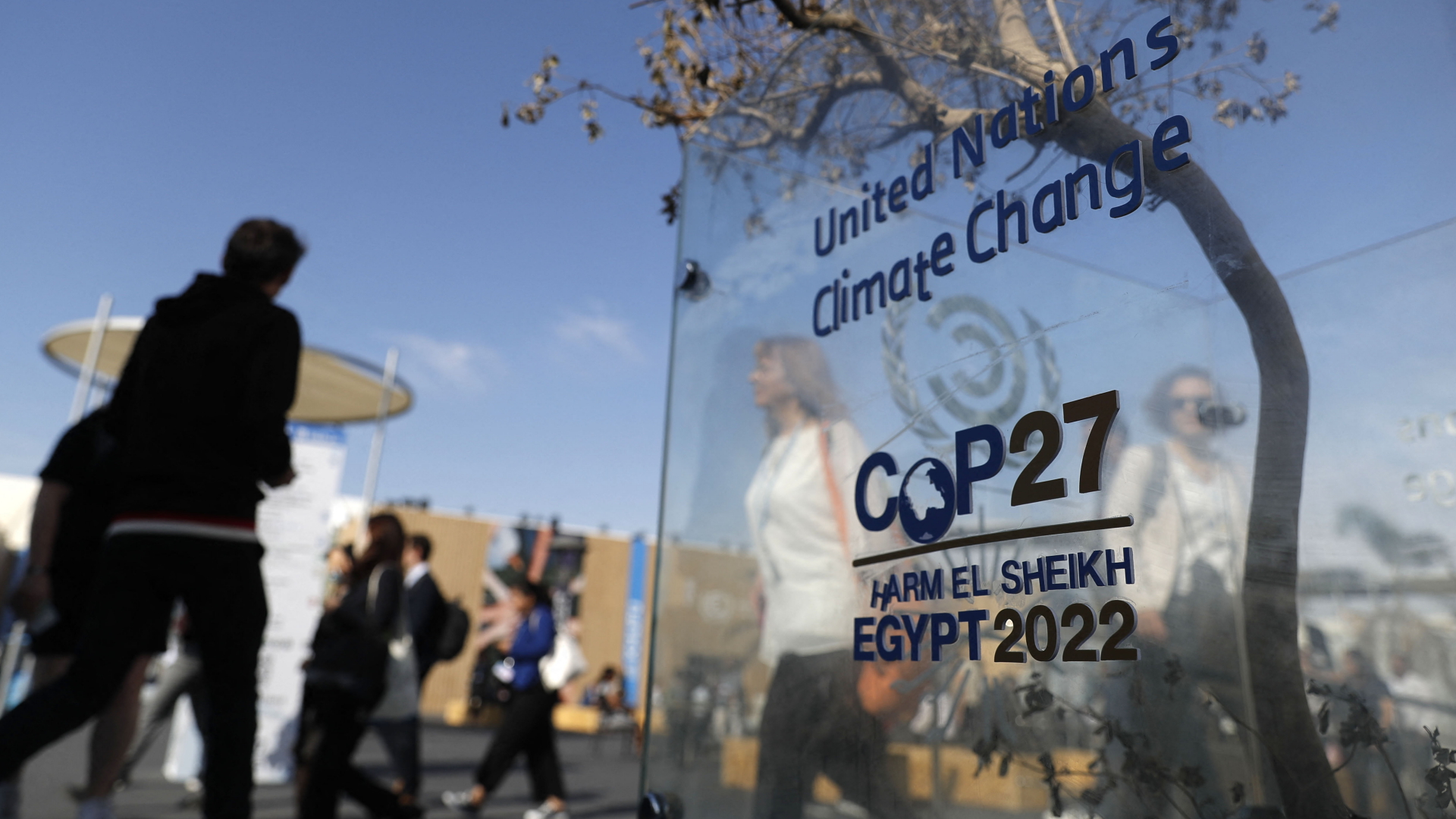 Menschen laufen an einem durchsichtigen Schild mit der Aufschrift COP27 Egypt 2022 vorbei. | AFP