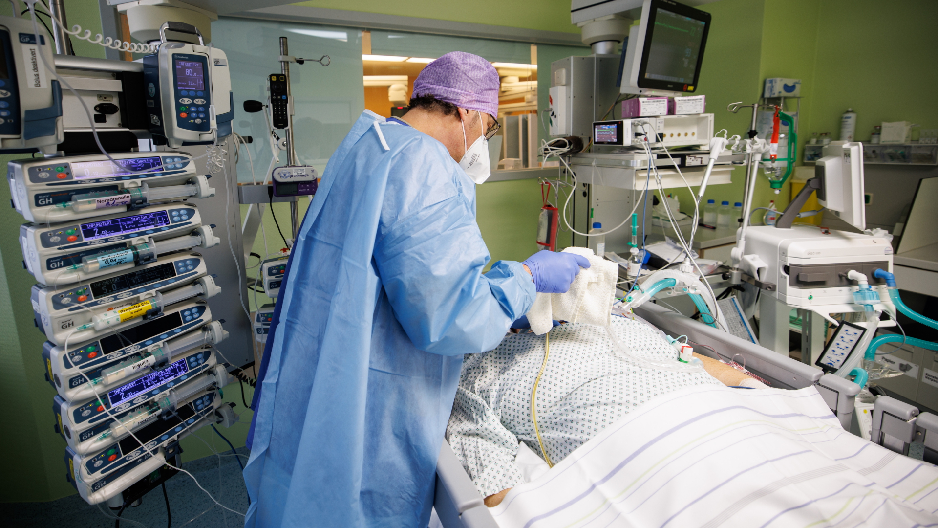 Ein Arzt arbeitet in Schutzkleidung in einem Intensivbett-Zimmer am Bett eines über einen Luftröhrenschnitt beatmeten Corona-Patienten. | dpa