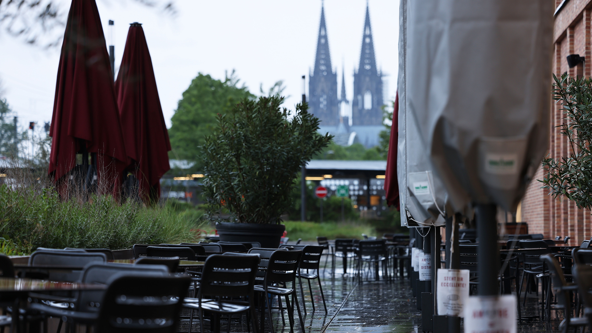 Stühle und Tische stehen vor einem Restaurant in Köln im Regen, im Hintergrund der Dom. | dpa