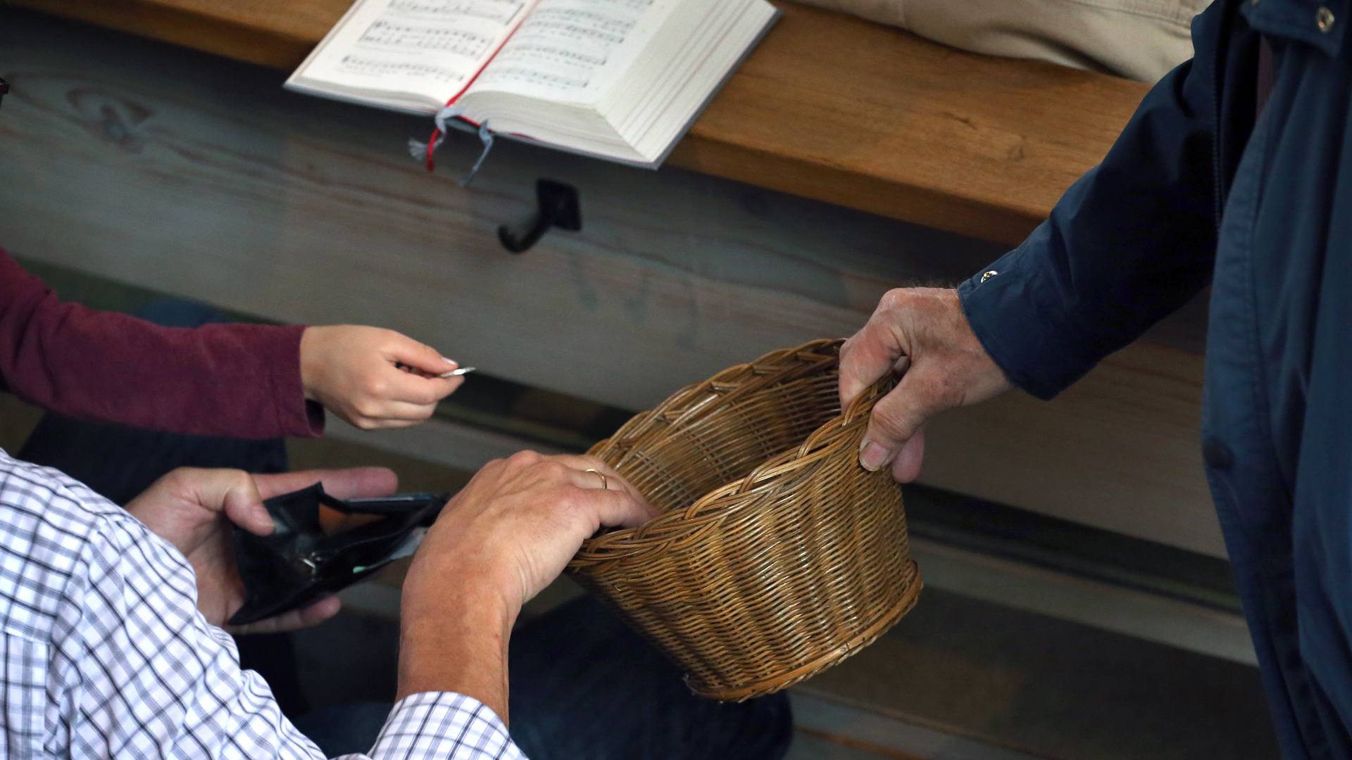 Besucher eines katholischen Gottesdienstes spenden Geld in einen herumgereichten Korb.