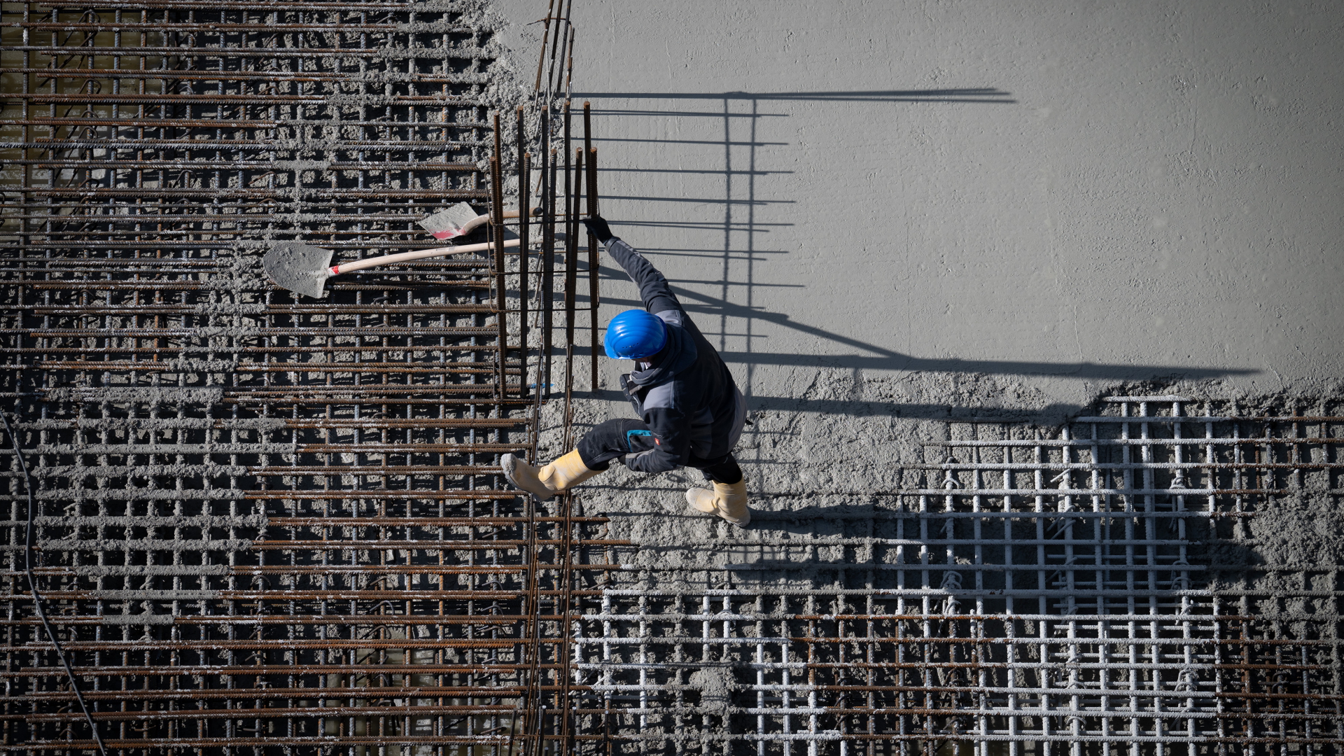 Ein Bauarbeiter läuft in Gummistiefeln über ein Gittergerüst. 