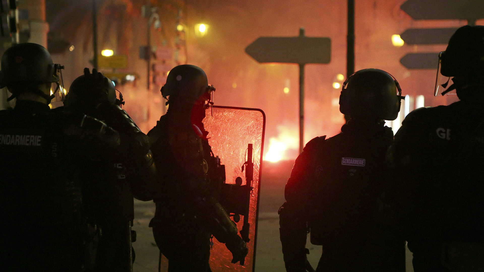 ranzösische Gendarmen stehen auf der Straße, während im Hintergrund ein Feuer brennt.  | dpa