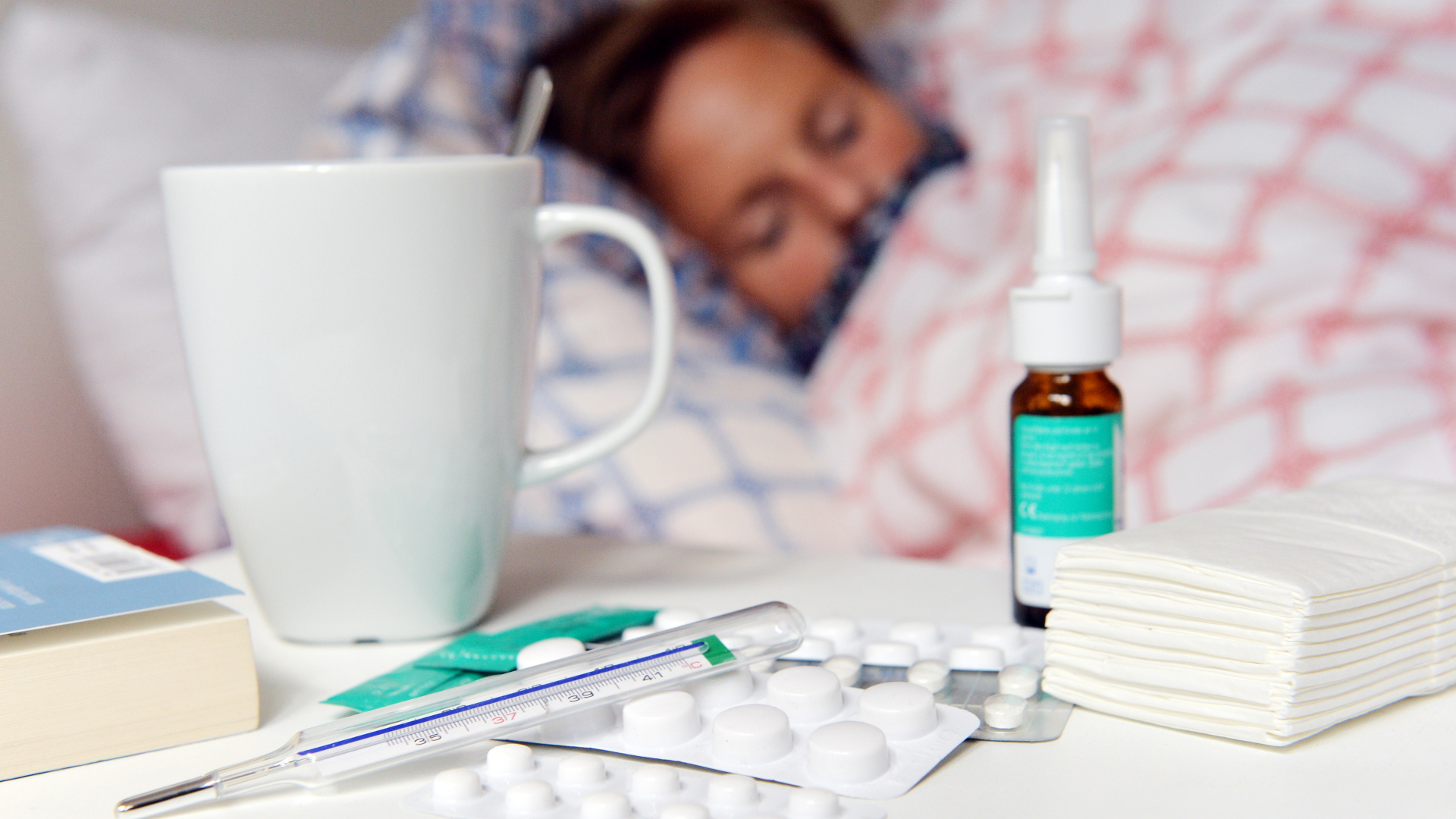 Fieberthermometer, Medikamente und Teetasse stehen auf einem Nachttisch