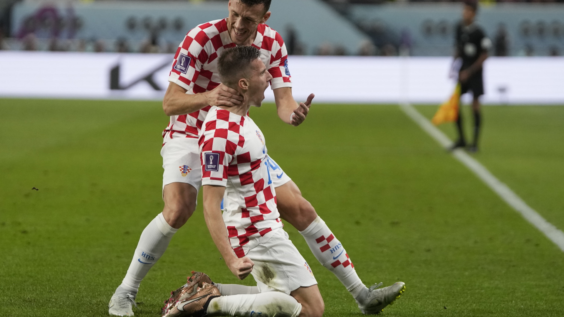 Der kroatische Nationalspieler Mislav Orsic kniet auf dem Rasen, sein Fußball-Kollege Ivan Perisic gratuliert zum erfolgreichen Torschuss gegen Marokko bei der Fußball-WM in Katar. | AP
