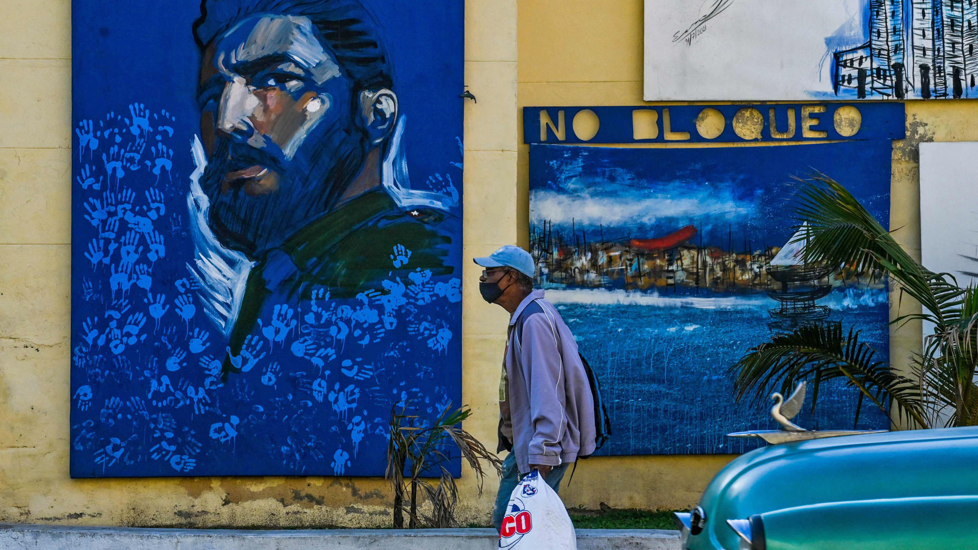 Ein Mann geht in Havanna an einer mit Bildern geschmückten Wand vorbei.