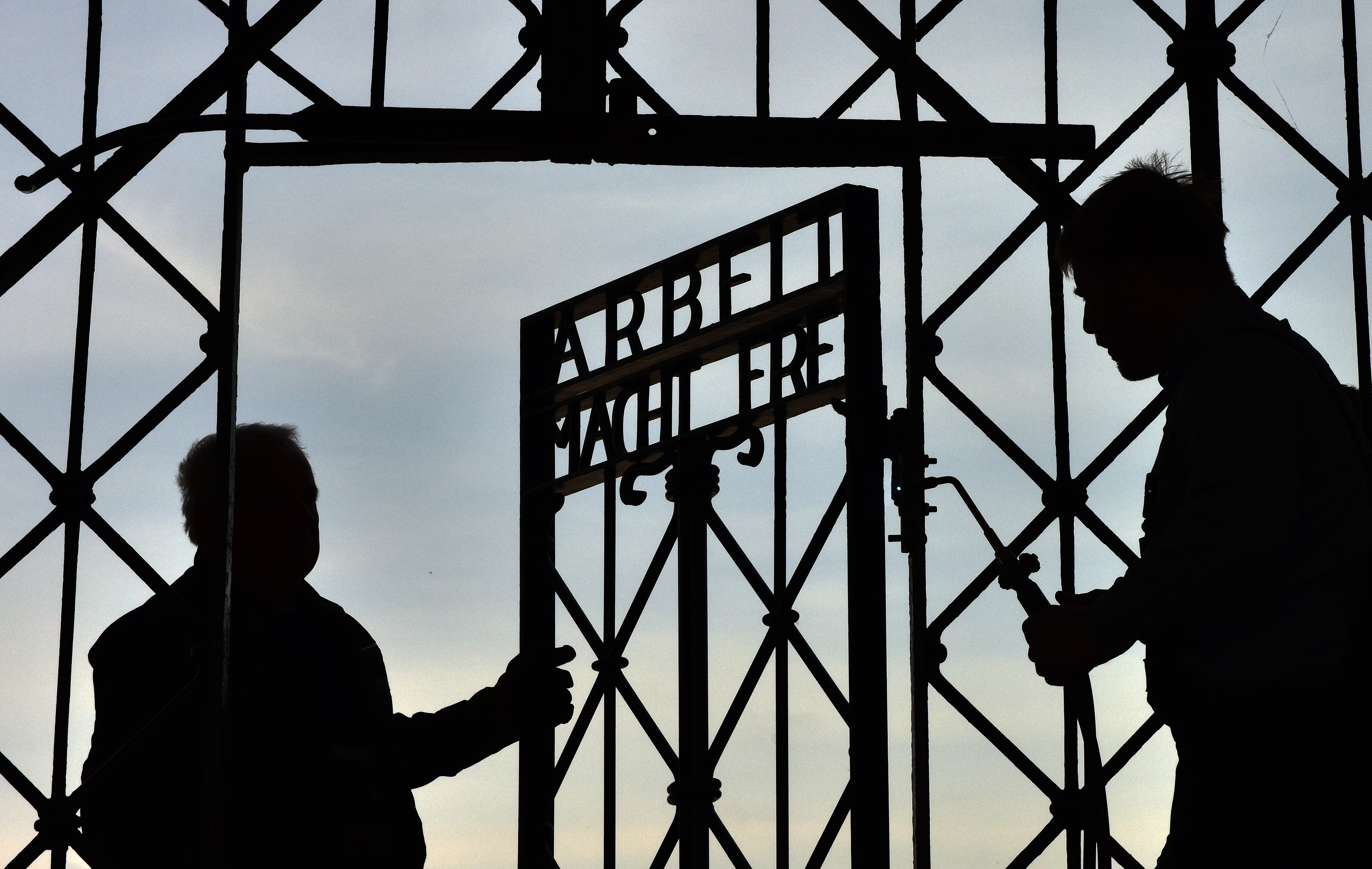 Zwei Männer öffnen ein Tor mit der Aufschrift "Arbeit macht frei". | dpa
