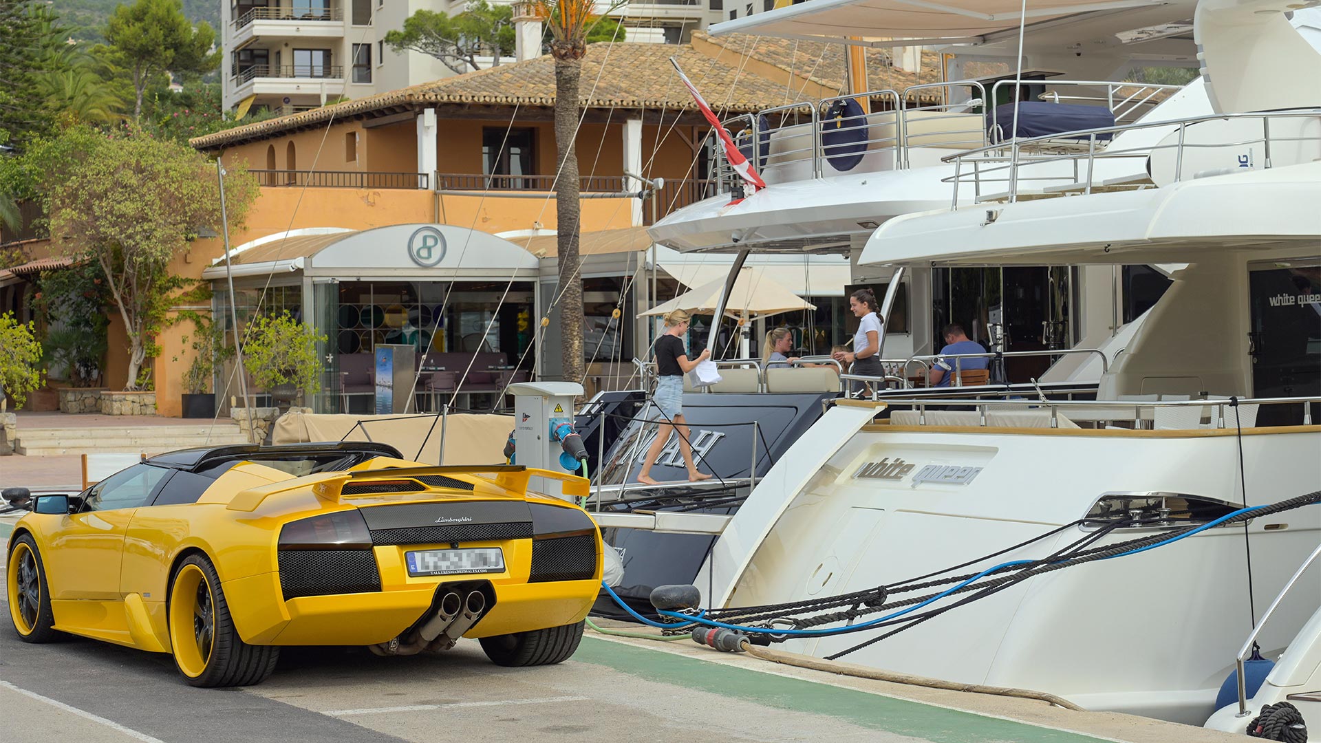 Ein gelber Lamborghini ist vor zwei Luxusjachten geparkt.