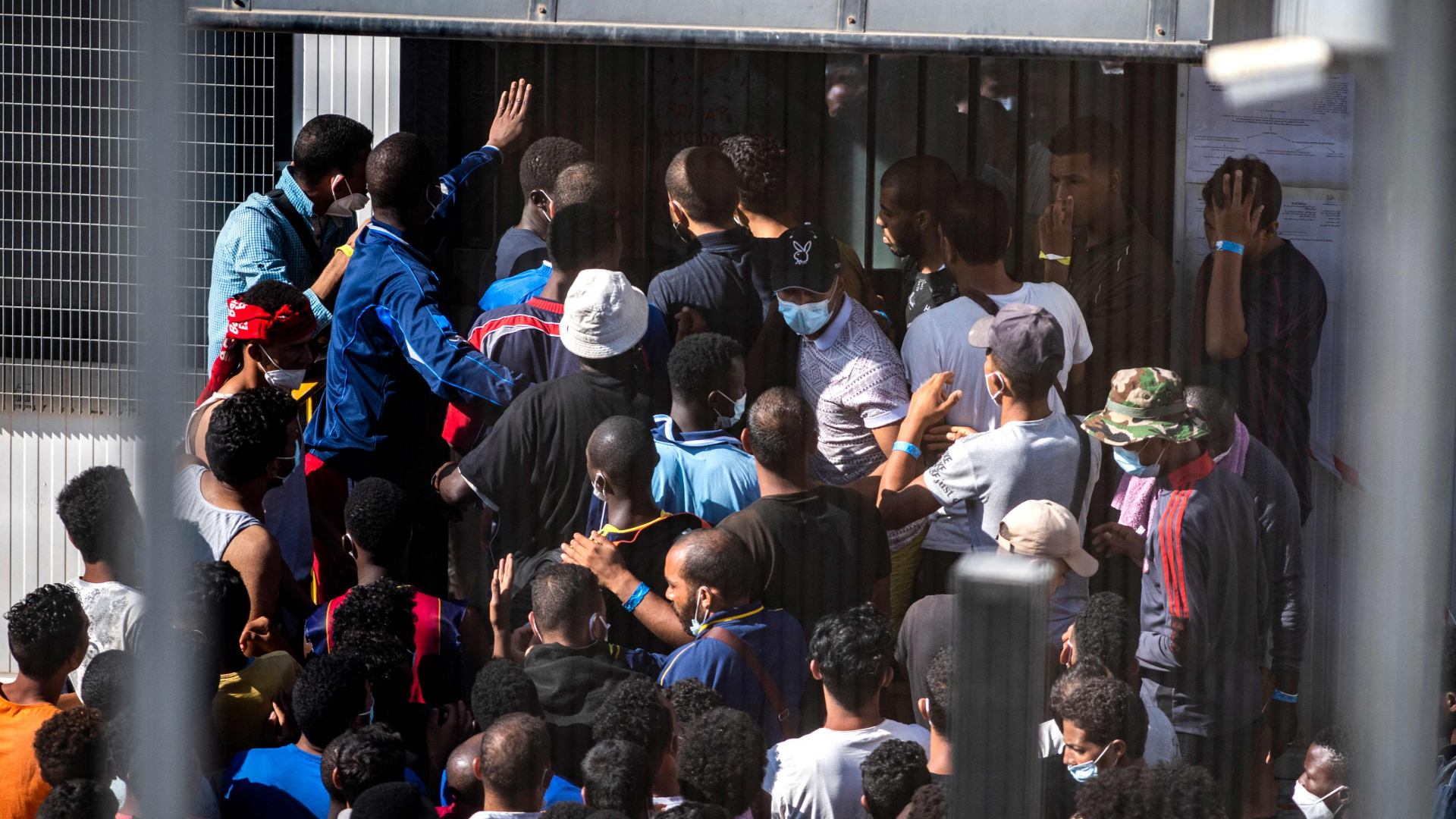 Menschen stehen Schlange vor einer Verwaltungseinrichtung im völlig überfüllten Flüchtlingscamp auf Lampedusa. | AFP