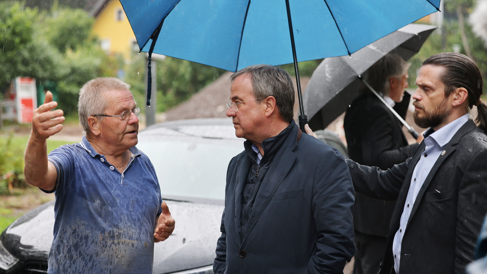 Ein Sicherheitsbeamter hält einen Regenschirm über Armin Laschet während er im Regen mit einem vom Hochwasser betroffenen Mann spricht.  | dpa