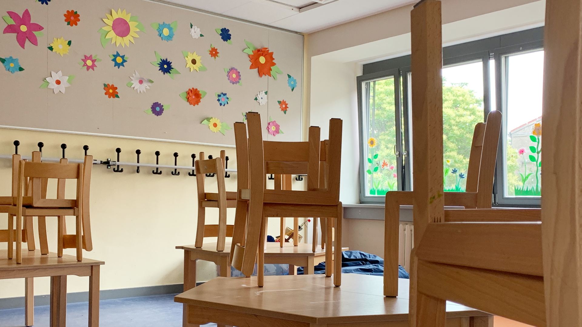 In einer Grundschule in Berlin stehen die Holzstühle auf den Tischen, im Hintergrund ist ein Wandbild mit vielen bunten Blumen. | dpa