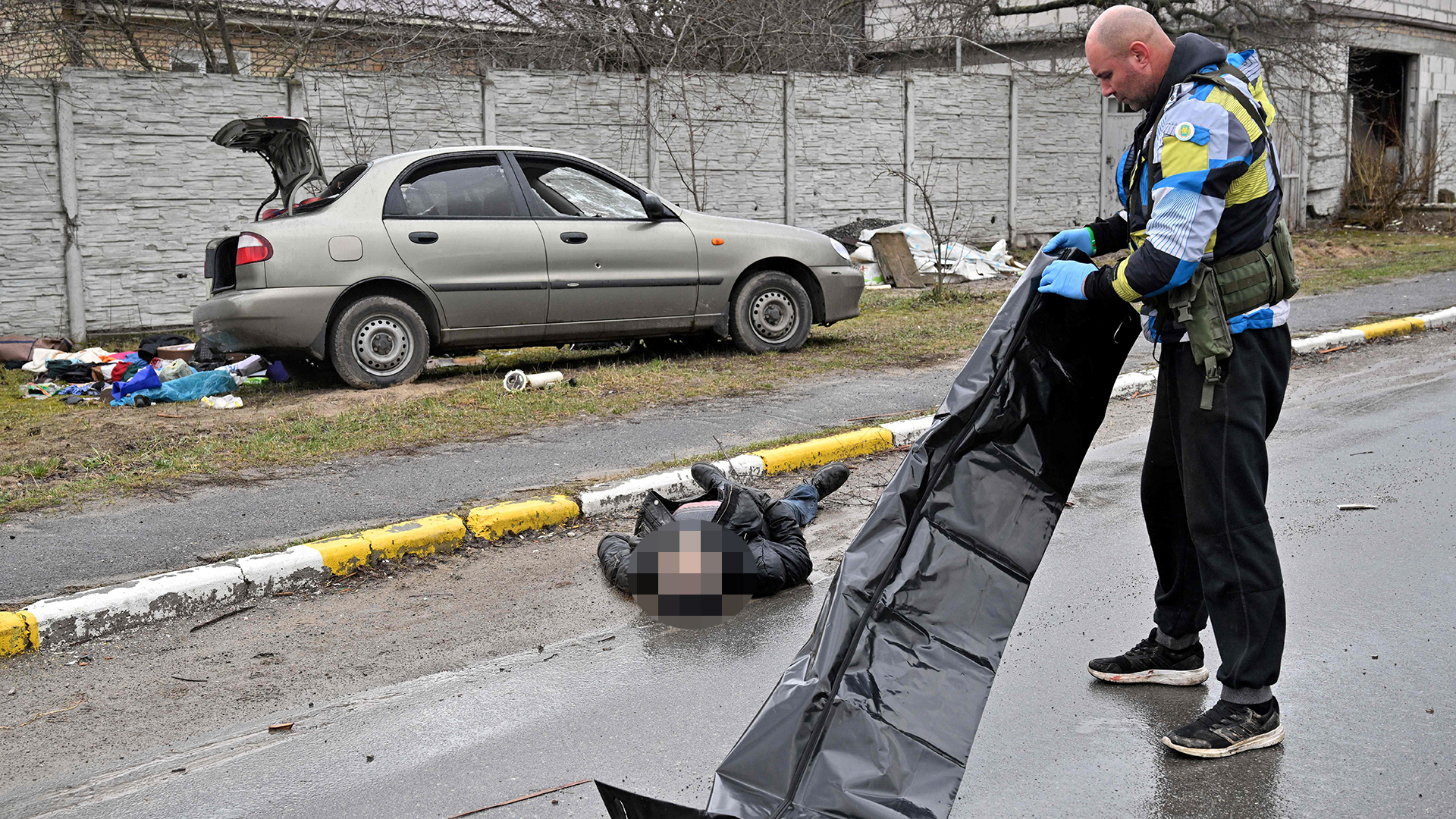Ein Mann kümmert sich um eine Leiche eines Menschen, die in Butscha auf einer Straße liegt. | AFP