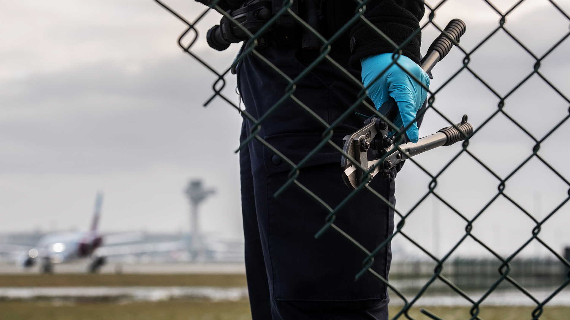 Eine Beamtin der Bundespolizei steht mit einem Bolzenschneider am Zaun eines  Flughafens. | dpa