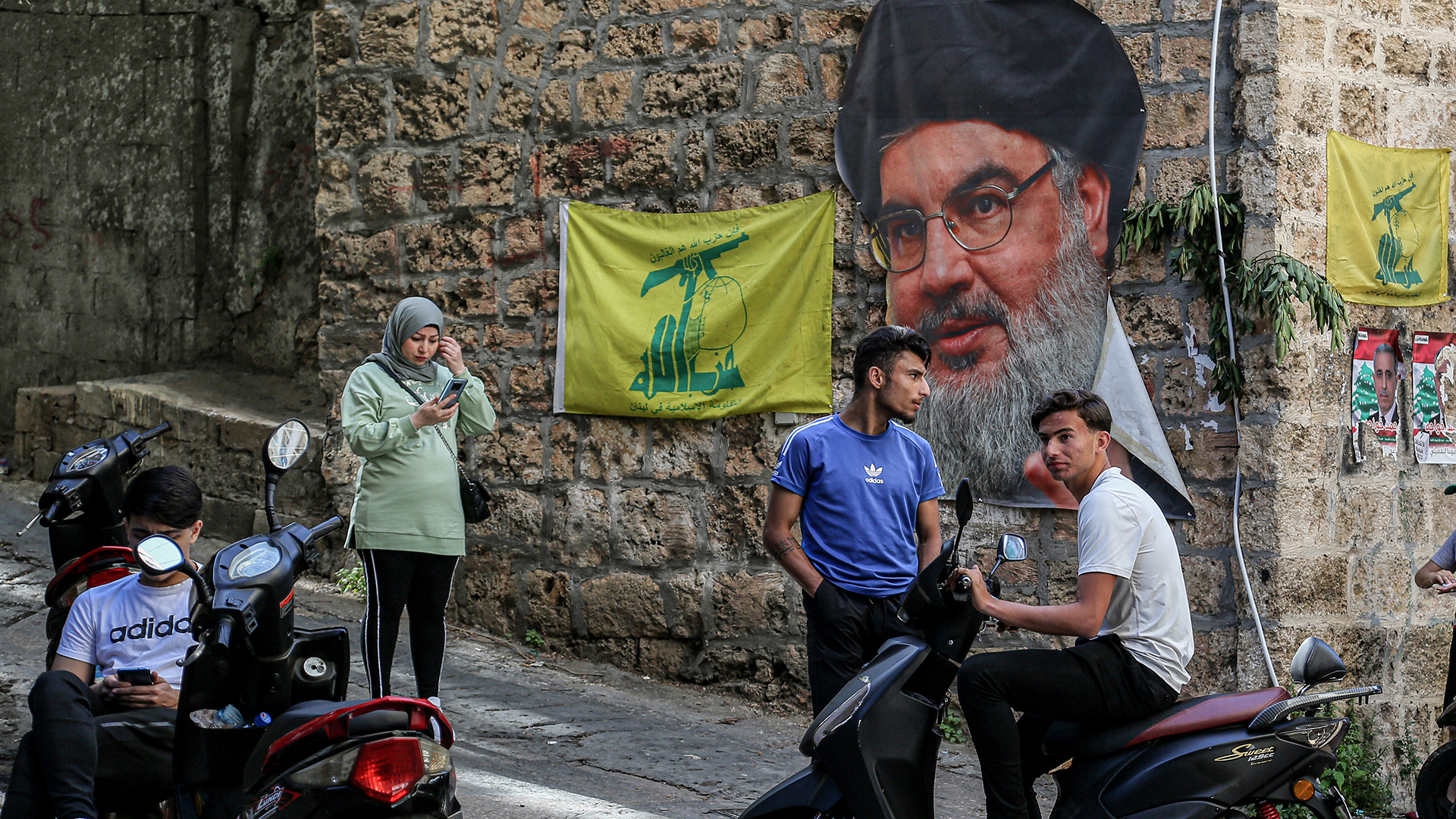 Junge Menschen auf einer Straße vor dem Bild des Hisbollah-Führers Nasrallah und Fahnen. | dpa
