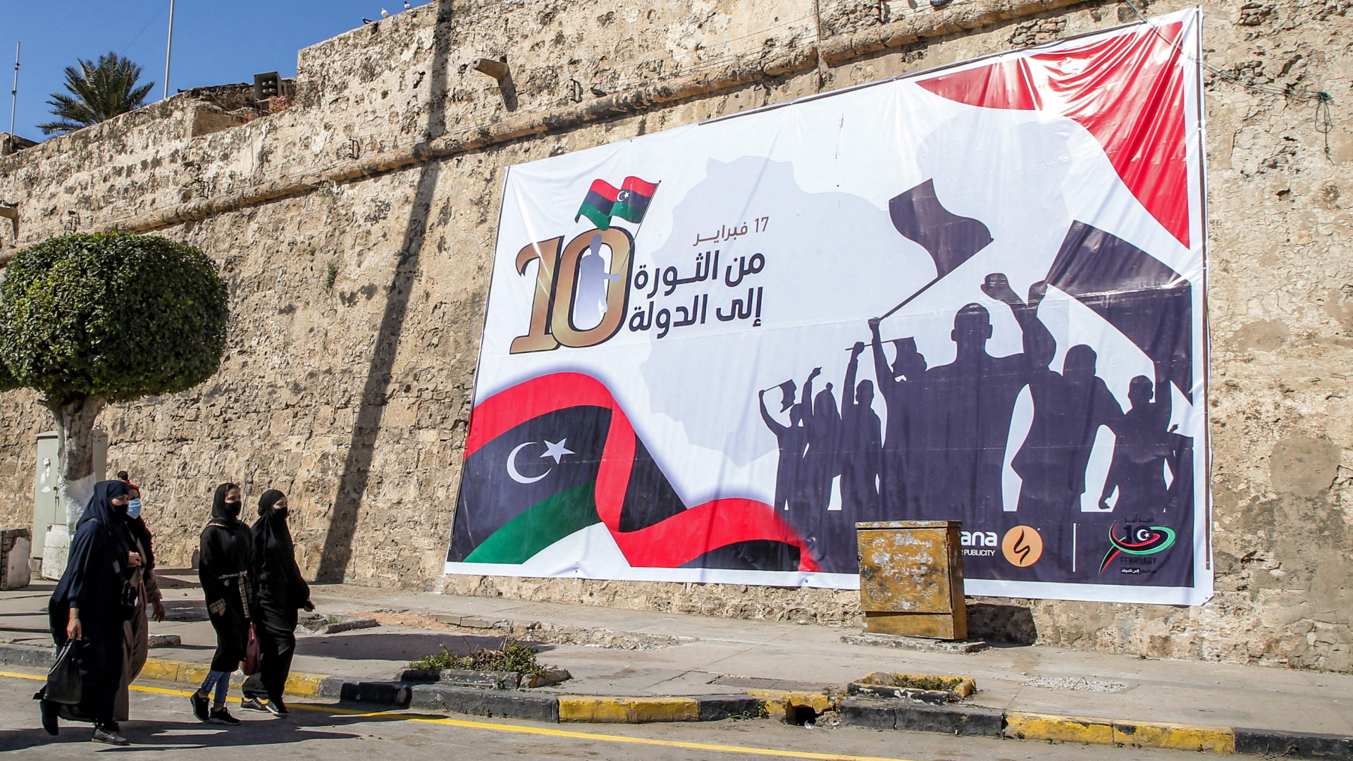 Frauen gehen in Tripolis an einem Plakat vorbei, auf dem steht: "17. Februar - von der Revolution zum Staat". | AFP