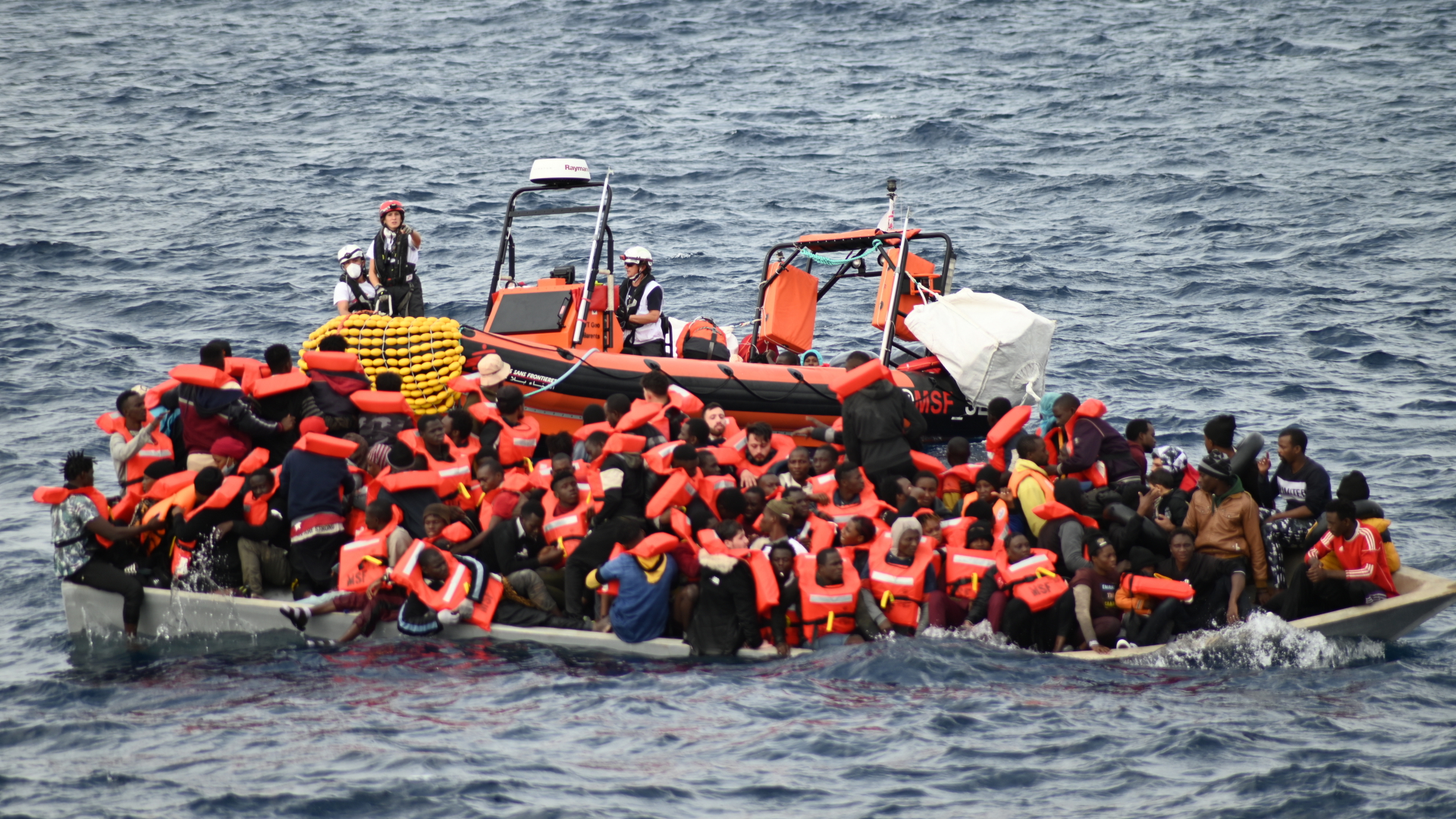  Ein Rettungsboot schwimmt hinter einem mit Migranten besetzten Boot im Mittelmeer.  | dpa