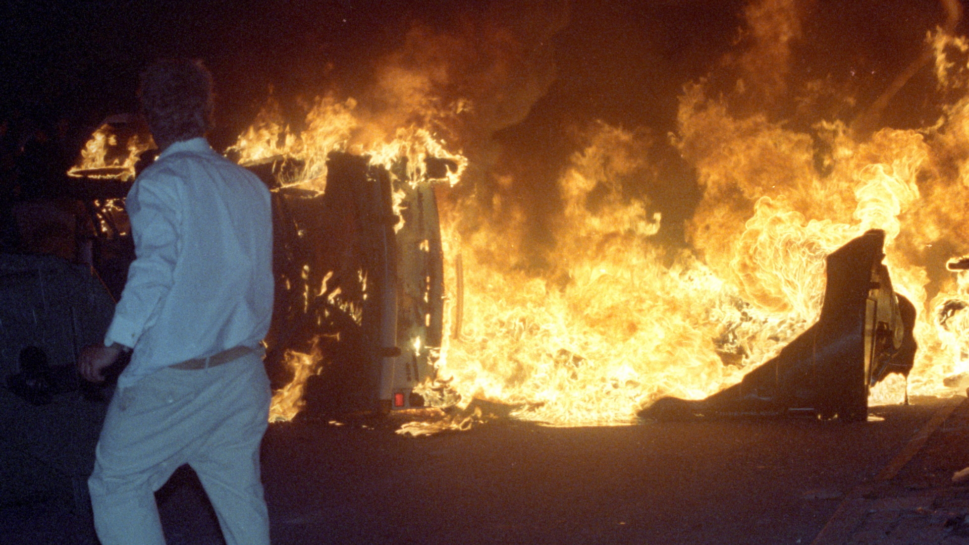 Ein Mann steht am 27.08.1992 vor einem brennenden Pkw auf einer Straße am zentralen Asylbewerberheim von Mecklenburg-Vorpommern in Rostock-Lichtenhagen.  | dpa