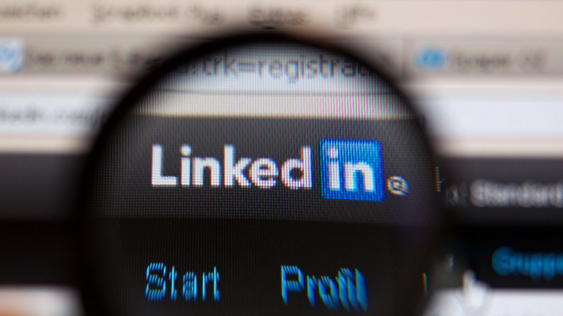 Das Logo des Karriere-Netzwerks LinkedIn ist unter einer Lupe auf einem Computermonitor zu sehen.
