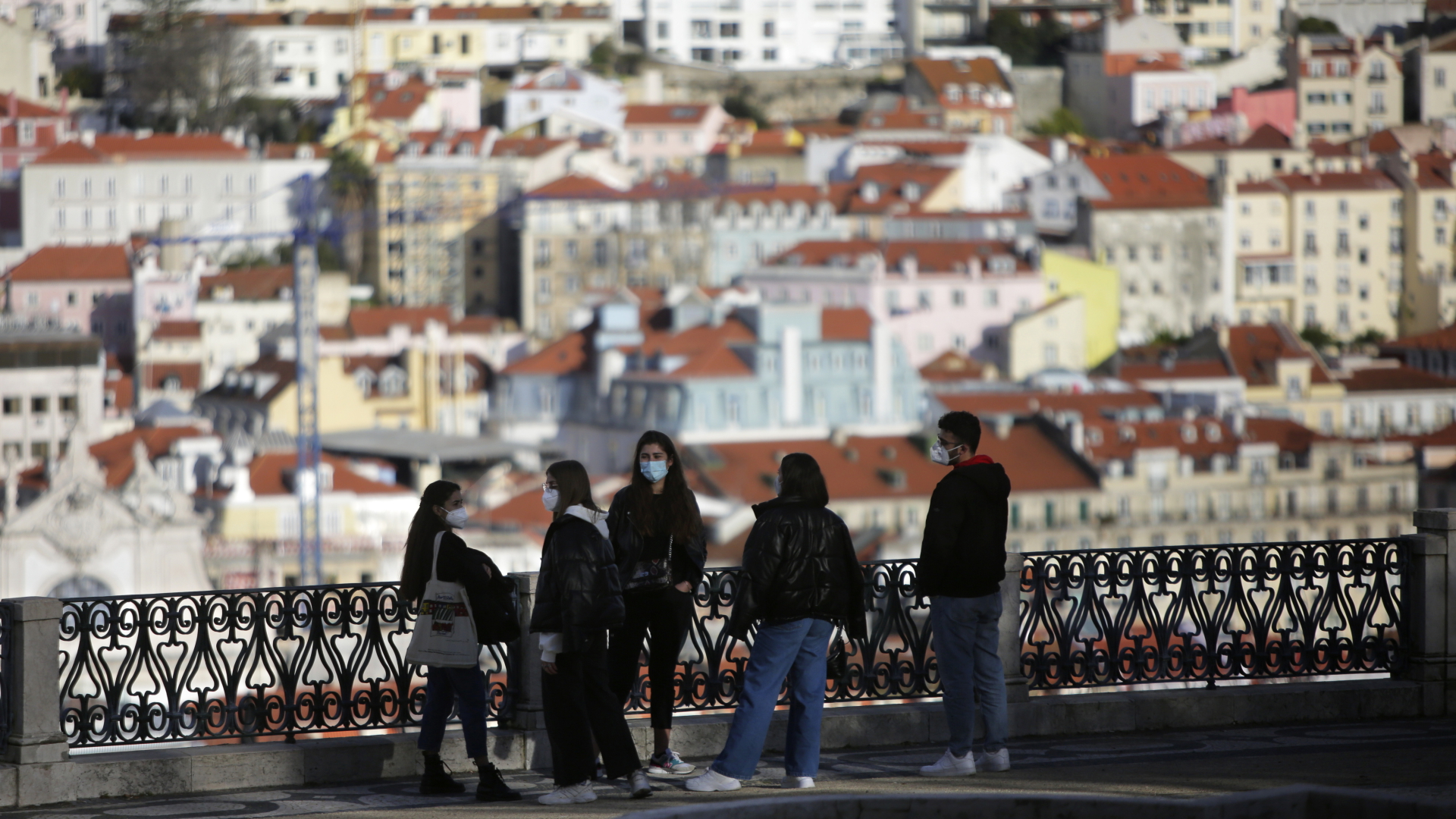 Eine Gruppe junger Menschen mit Mund-Nasen-Schtuz steht an einem Aussichtspunkt mit Blick auf die Altstadt von Lissabon (Archivbild vom 11. März 2021) | dpa