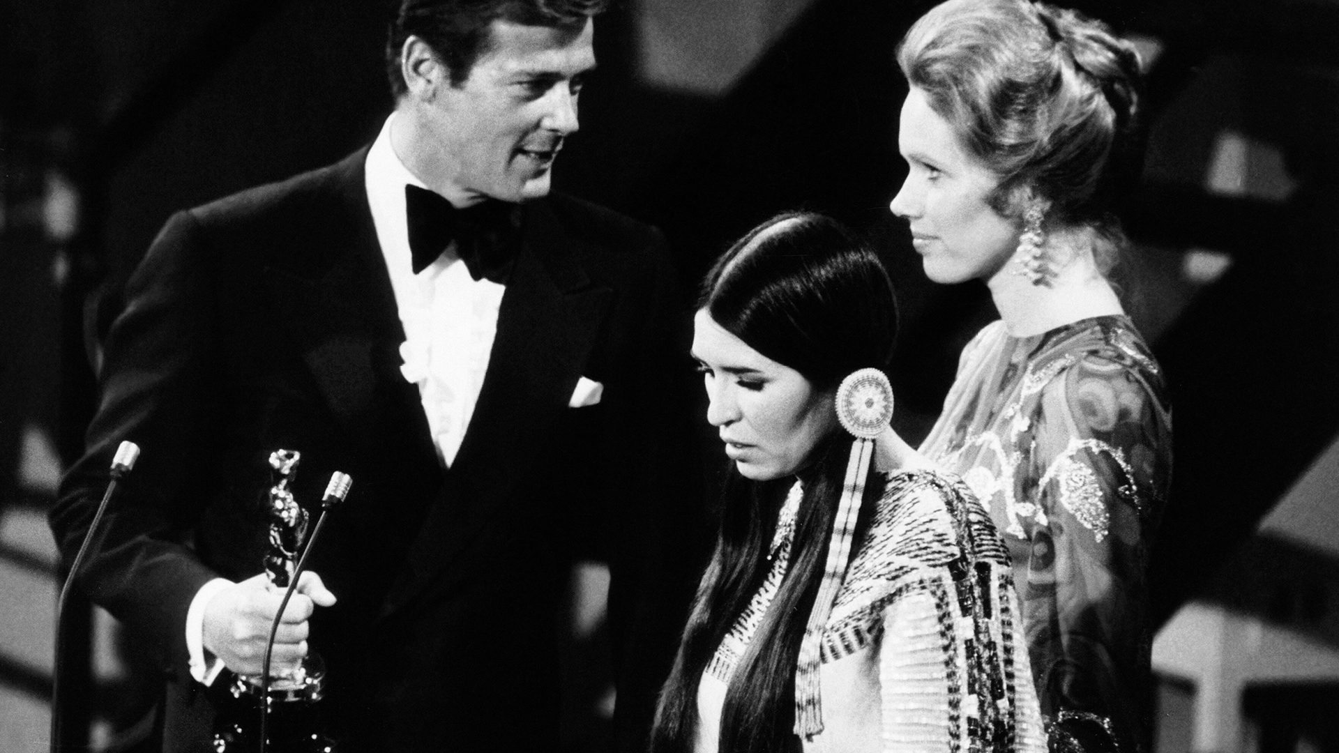 Roger Moore, Liv Ullmann und Sacheen Littlefeather bei der Oscarverleihung 1973. | imago images/Everett Collection