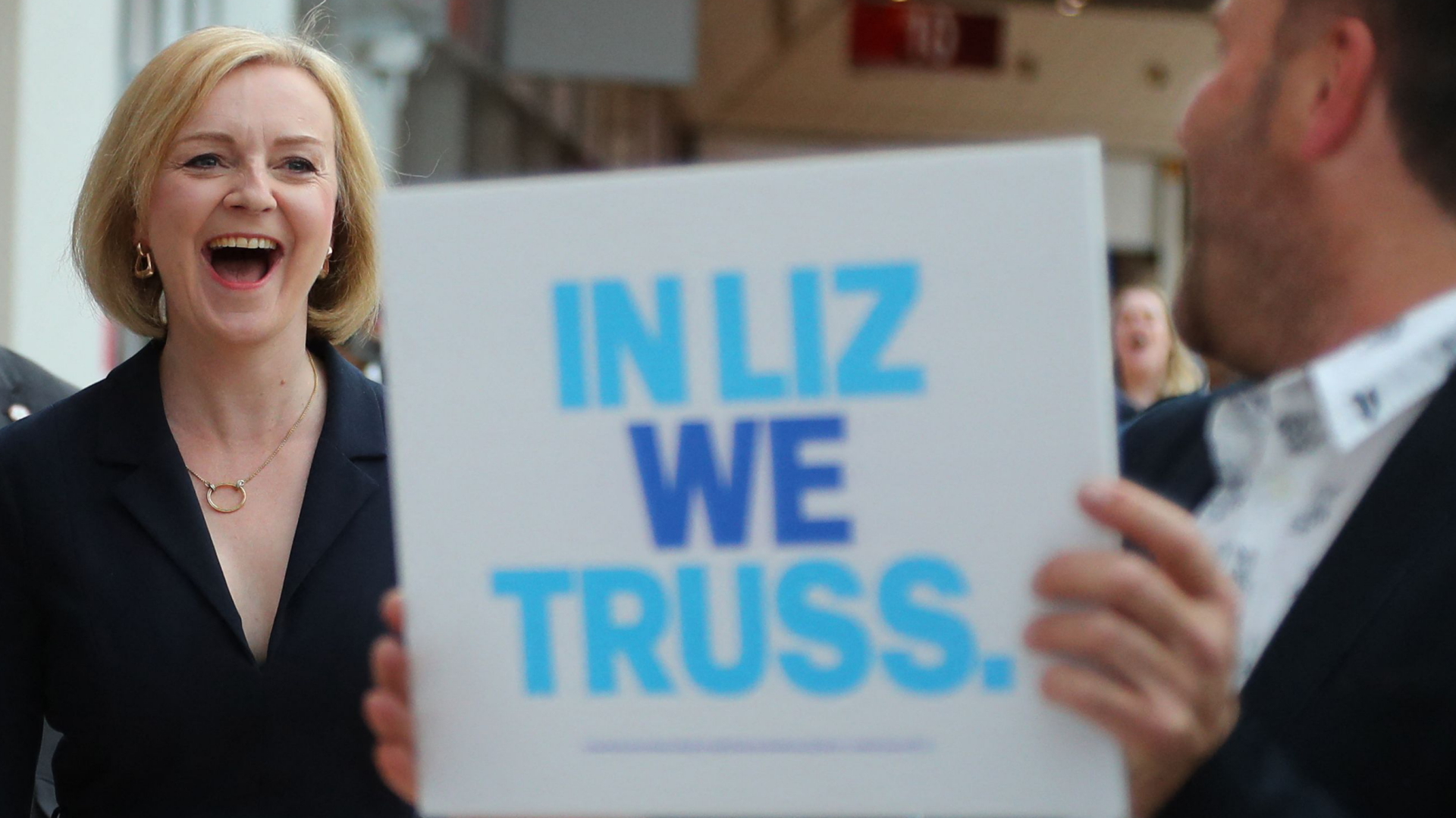 Liz Truss neben einem Unterstützer, der ein Wahlplakat hochhält | AFP