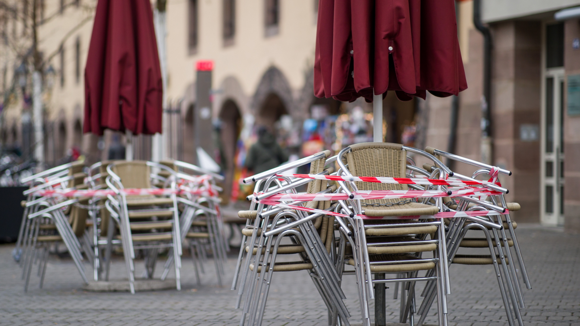 Stühle eines Restaurants stehen mit Absperrband zusammengebunden auf dem Gehweg.