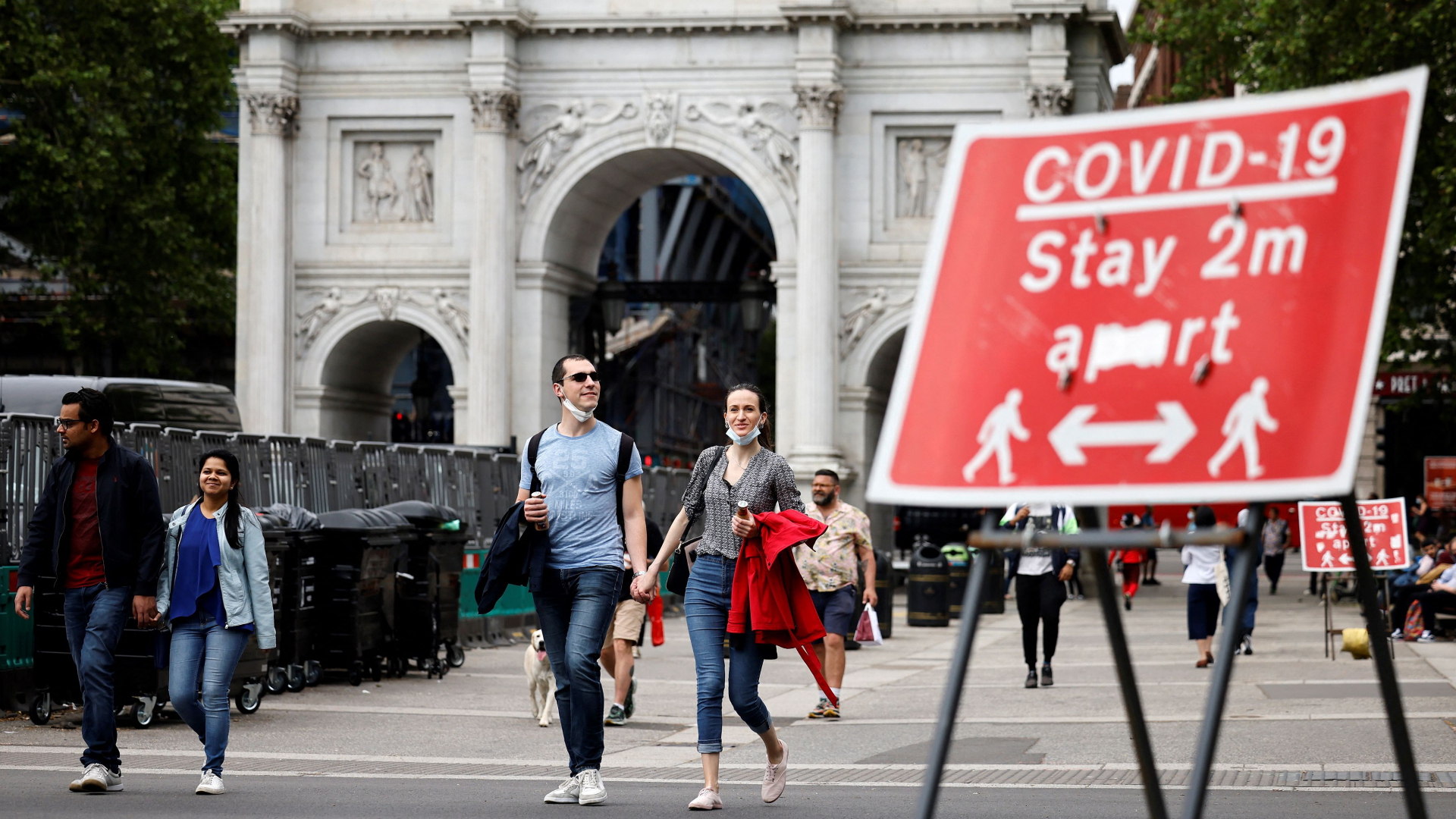Fußgänger vor der Marble Arch in London gehen an einem Schild vorbei, das auf die Einhaltung der Abstandsregeln hinweist. | AFP