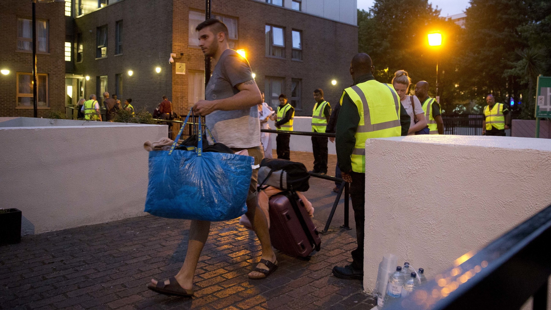 Ein Mann mit Gepäck verlässt bewacht von Sicherheitskräften ein evakuiertes Hochhaus.  | AP
