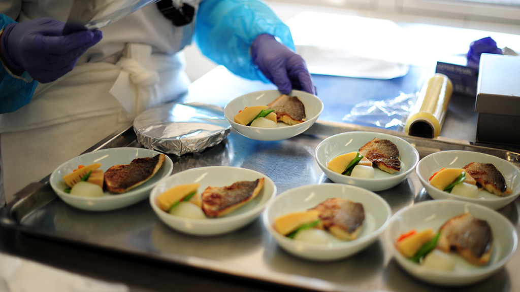 Eine Frau stellt Schalen mit Fisch-Mahlzeiten auf ein Tablett in der Produktion der LSG Sky Chefs