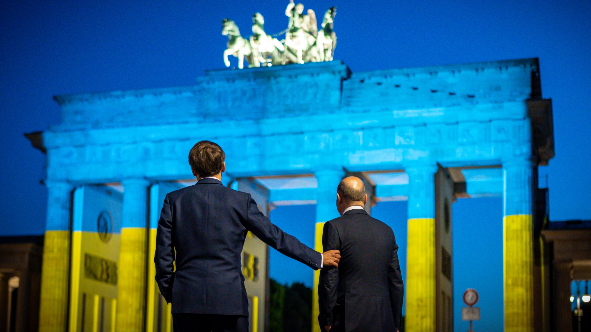 Emmanuel Macron und Olaf Scholz vor dem Brandenburger Tor, das in den Farben der Ukraine erscheint. | dpa