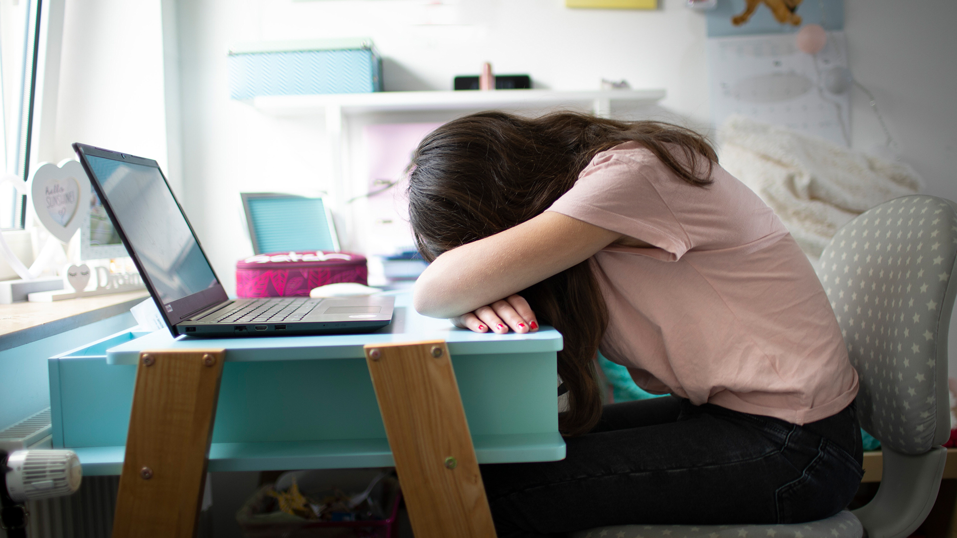 Ein Mädchen sitzt an einem Schreibtisch und hat ihren Kopf auf die Arme gelegt. | picture alliance / photothek