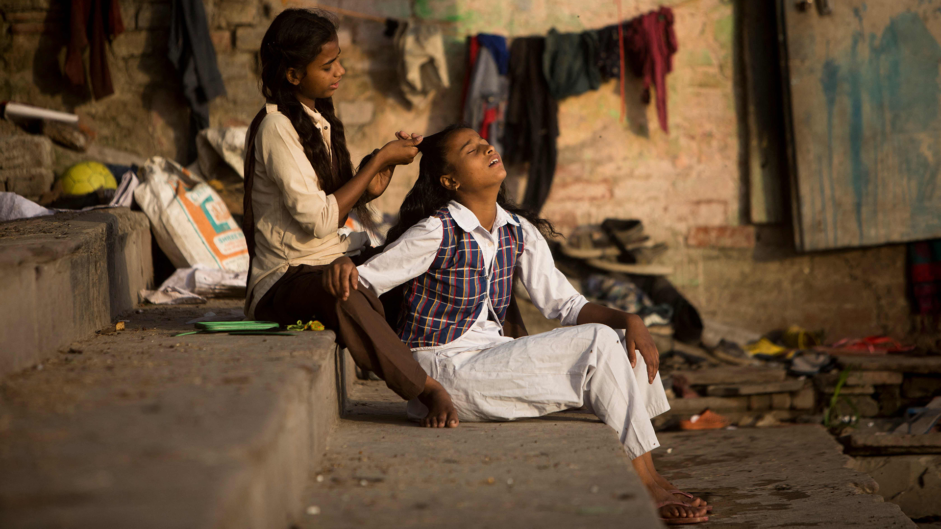 Ein Mädchen macht die Haare ihrer Schwester, während sie sich in Neu-Delhi (Indien) auf den Schulbesuch vorbereiten. | AFP