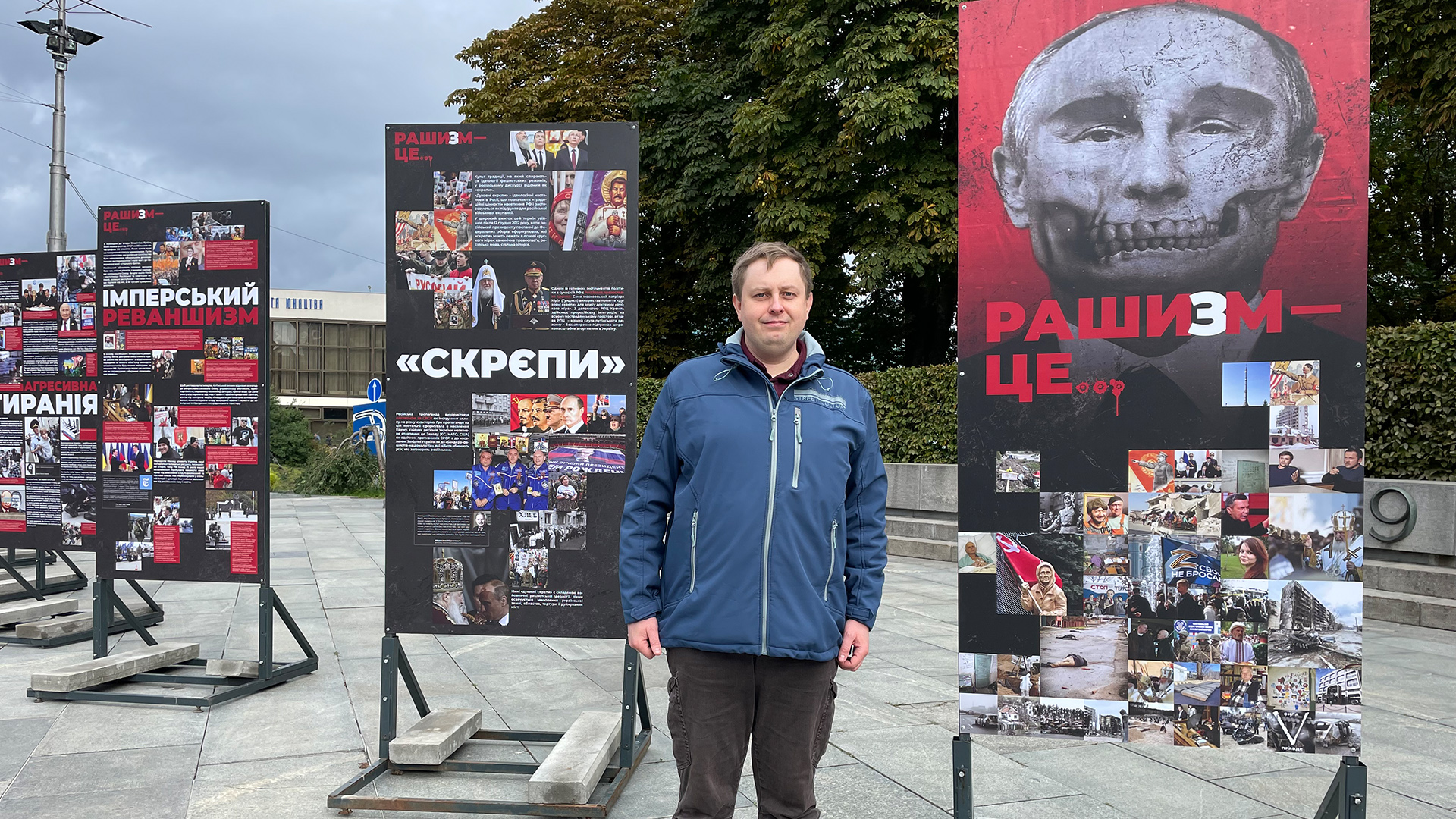 Maksim Majorow vor einer Stellwand mit einem Bild von Putin als Totenkopf verfremdet und der Aufschrift "Raschism"  | Andrea Beer
