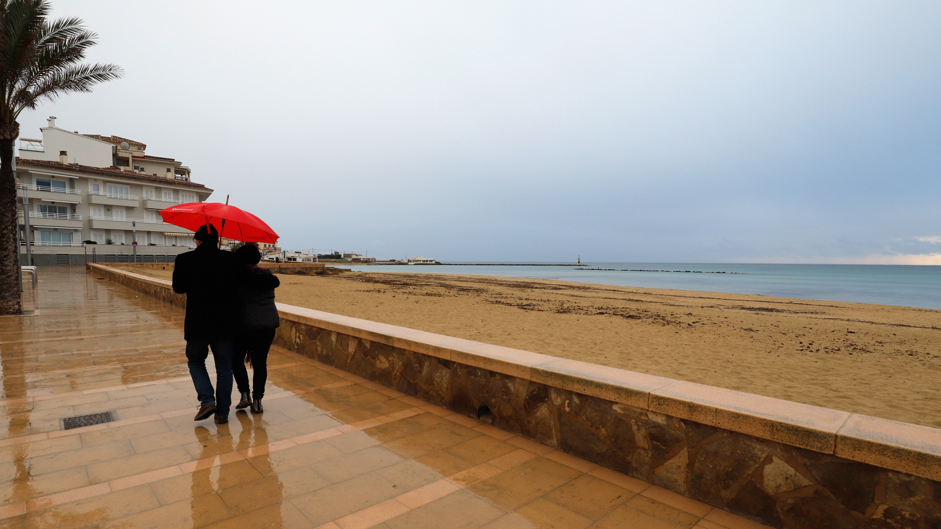 Ein Paar läuft unter einem roten Regenschirm an einem Regentag über die Promenade in Palma de Mallorca. | dpa
