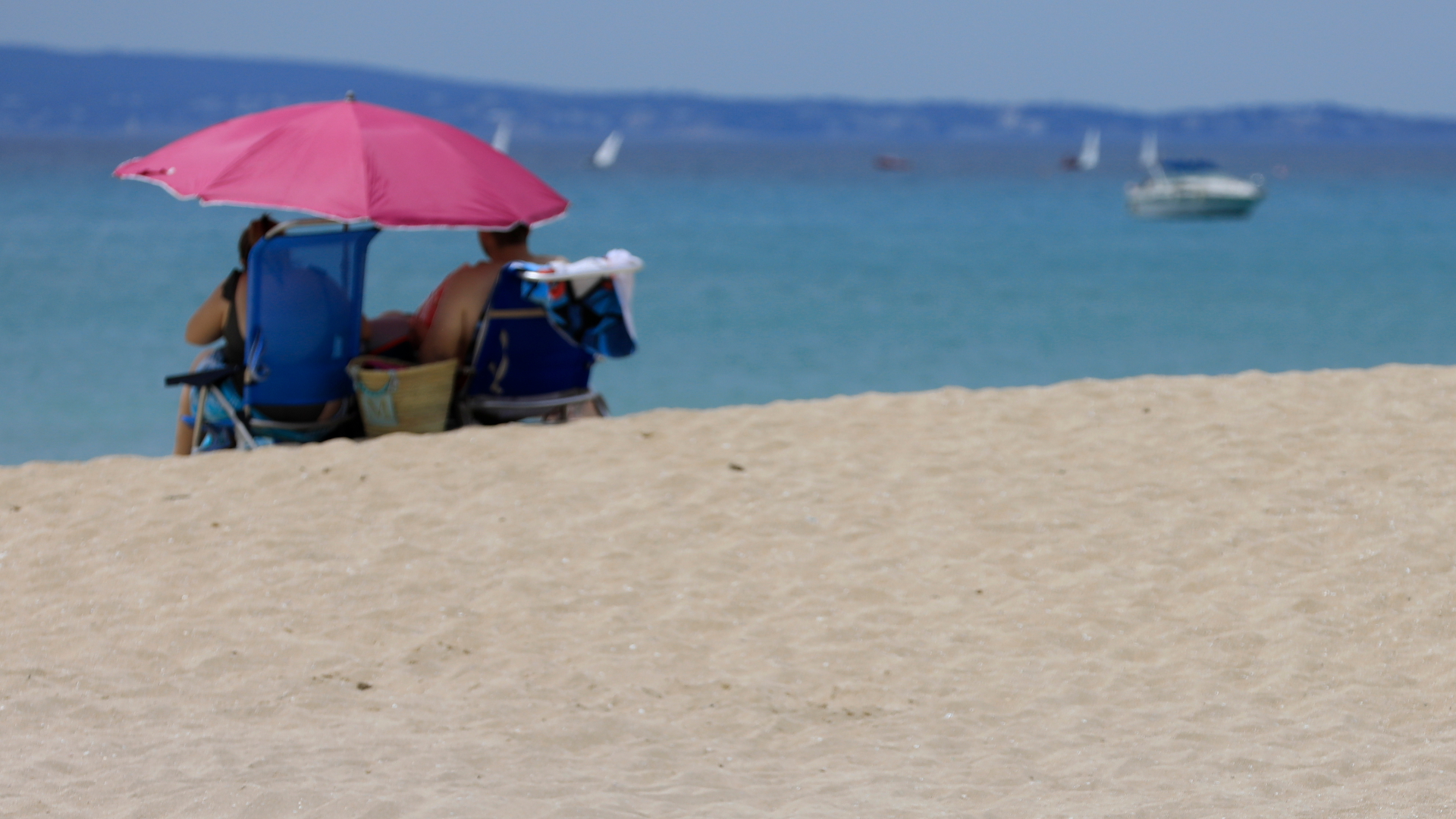 An einem Strand auf Mallorca sitzt ein Urlauberpärchen unter einem Sonnenschirm.