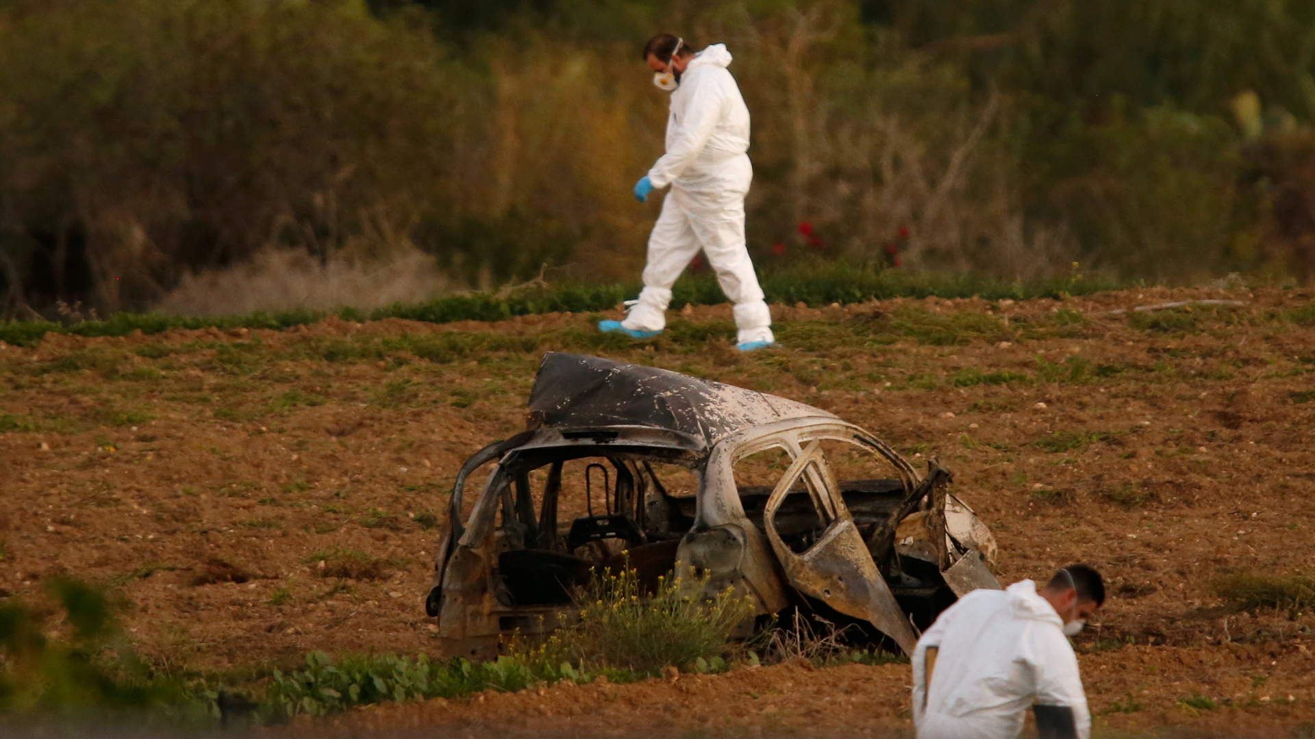 Ermittler in Schutzanzügen untersuchen die Gegend rund um das völlig ausgebrannte Autowrack, in dem Caruana Galizia ums Leben kam. | REUTERS