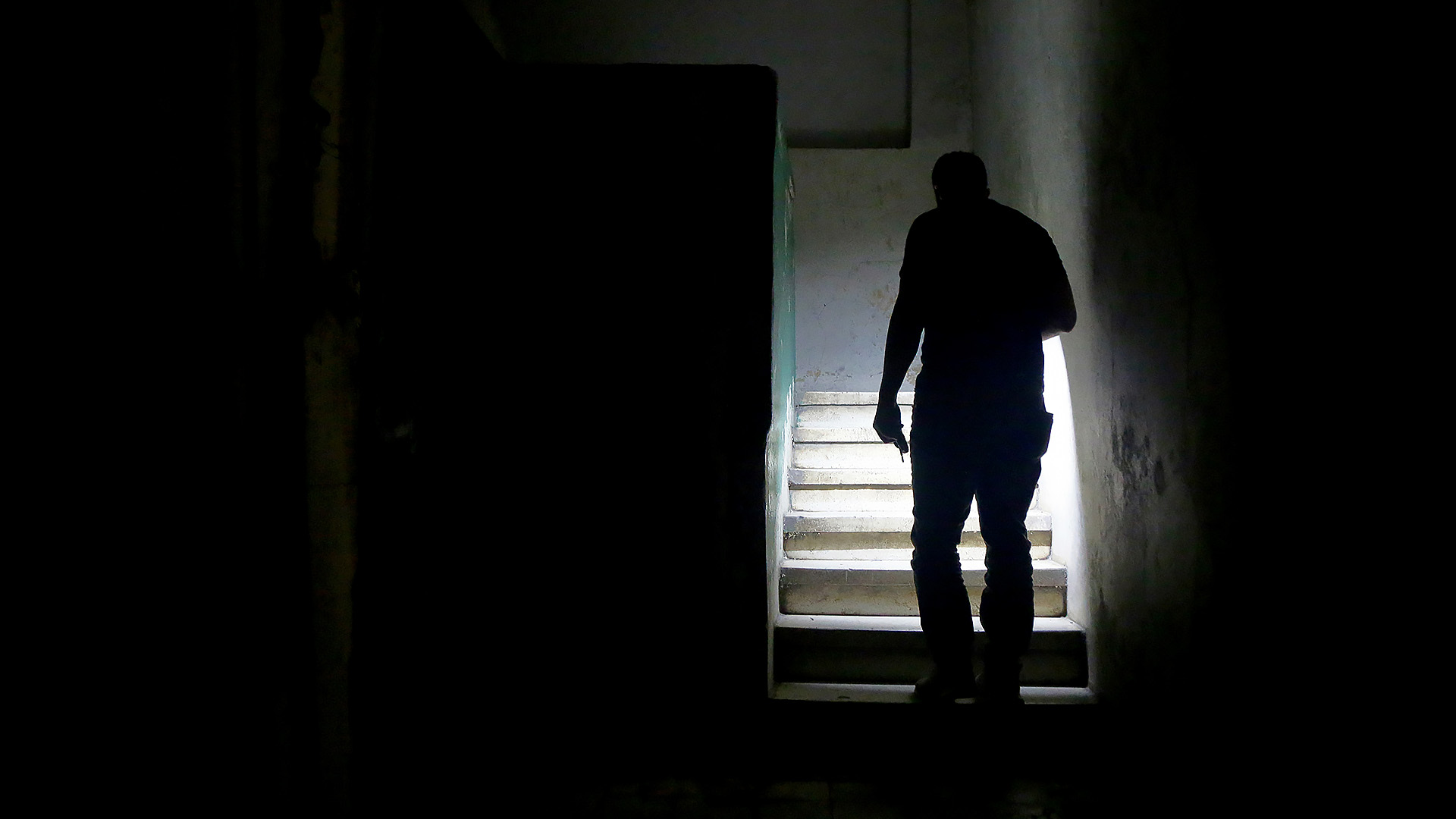Ein Mann steigt mit einer Taschenlampe während eines Stromausfalls die Treppe hoch.