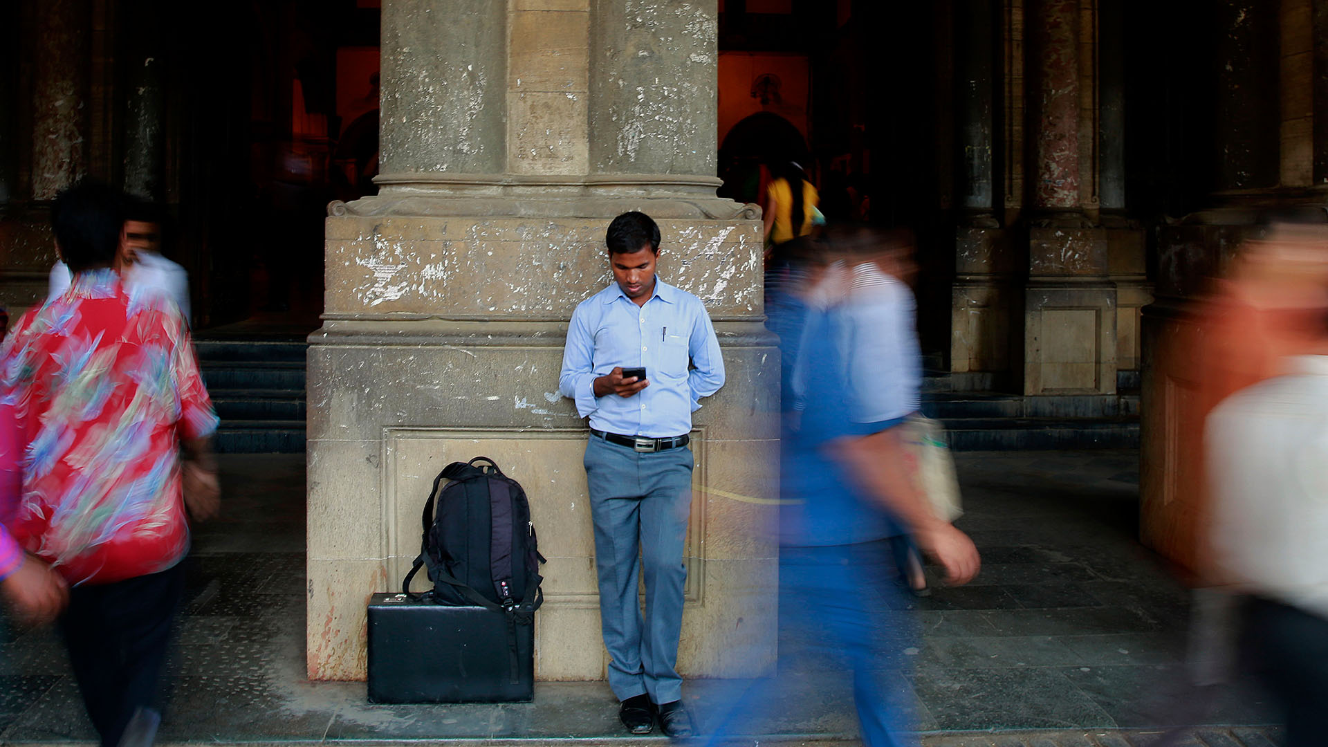 Ein Mann steht an einer Zugstation in Mumbai und schaut in sein Smartphone. | picture alliance / AP Photo