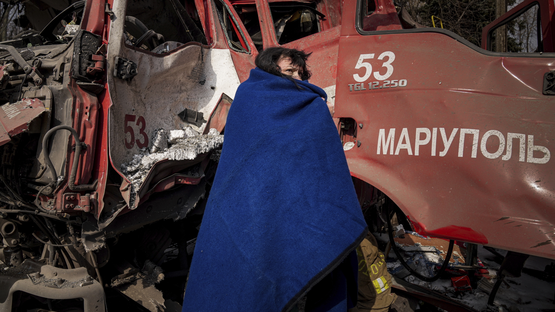 Eine Frau in Mariupol bedeckt sich mit einer Decke in der Nähe eines beschädigten Feuerwehrwagens nach einem Beschuss. | dpa