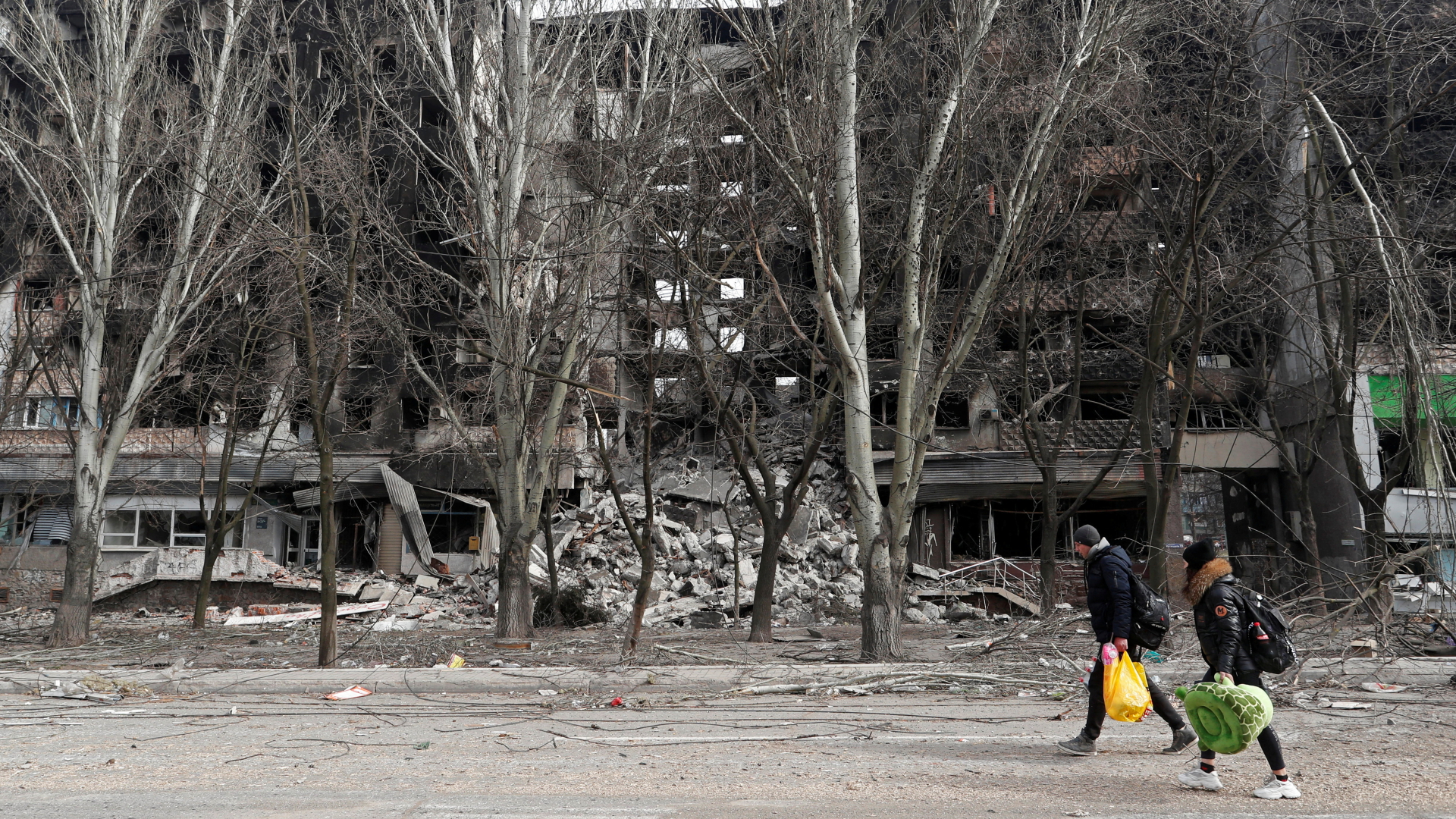 In Mariupol laufen Menschen über eine Straße vor zerstörten Gebäuden. | REUTERS
