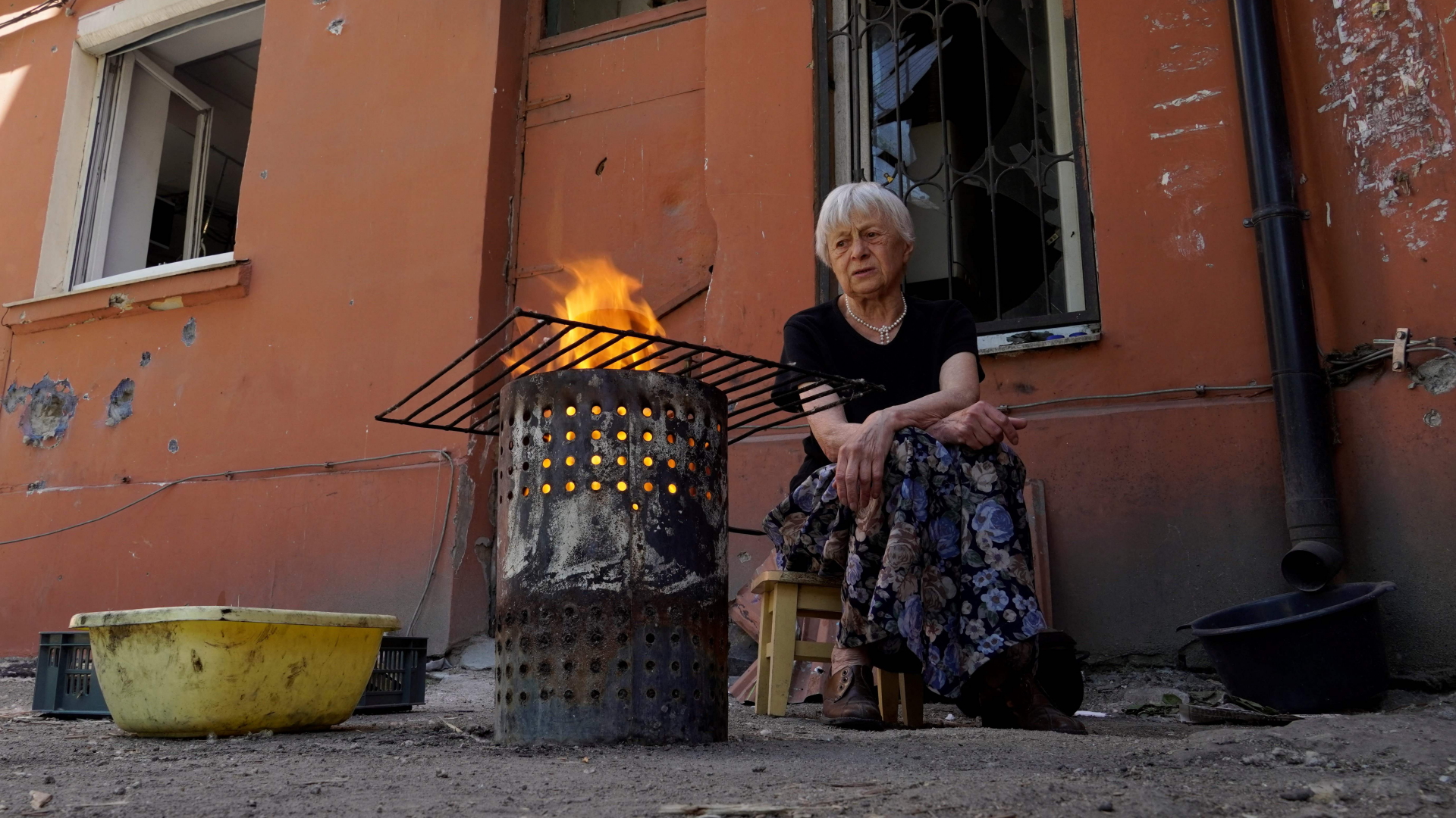 Eine ältere Frau kocht in Mariupol über einem offenen Feuer aus einer Tonne (Bild vom 4.06.2022). | AFP