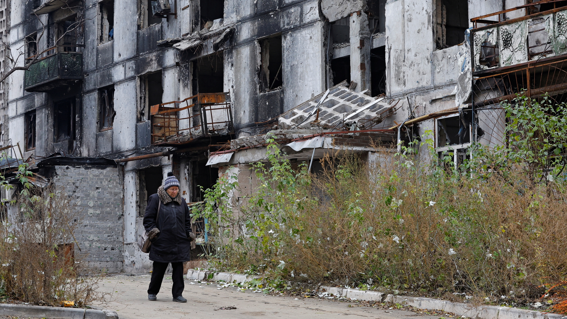 Eine Bewohnerin von Mariupol läuft vor einem zerstörten Wohngebäude entlang. | REUTERS