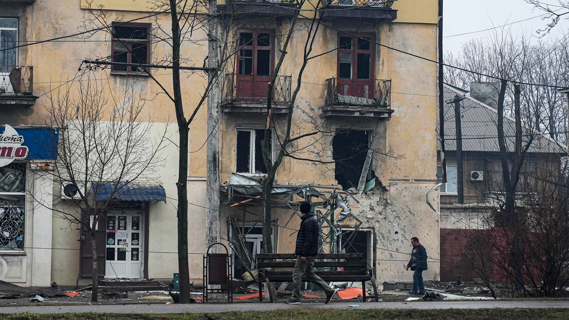 Personen gehen auf einer Straße an einem Wohnhaus in Mariupol vorbei, das Schäden nach einem Beschuss aufweist. | picture alliance/dpa/AP