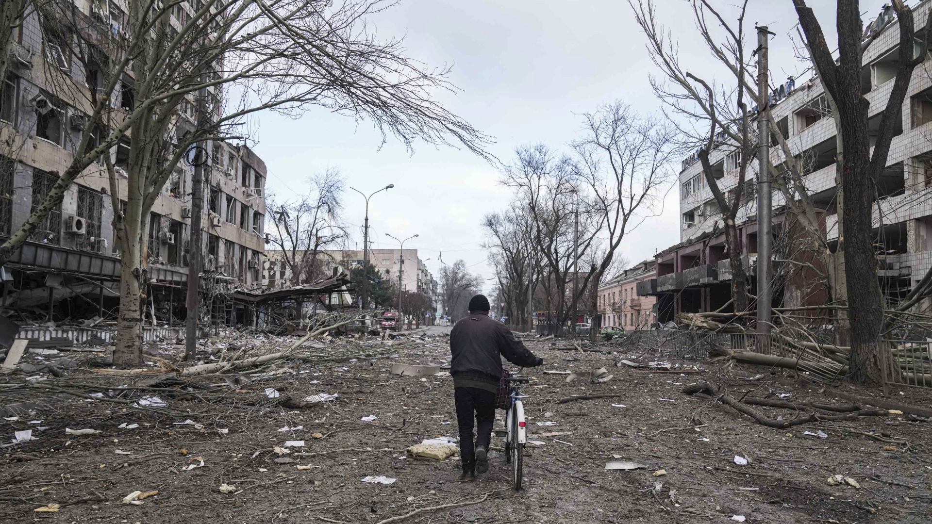 Ein Mann geht mit einem Fahrrad auf einer Straße in Mariupol, die durch einen Beschuss beschädigt wurde.  | dpa