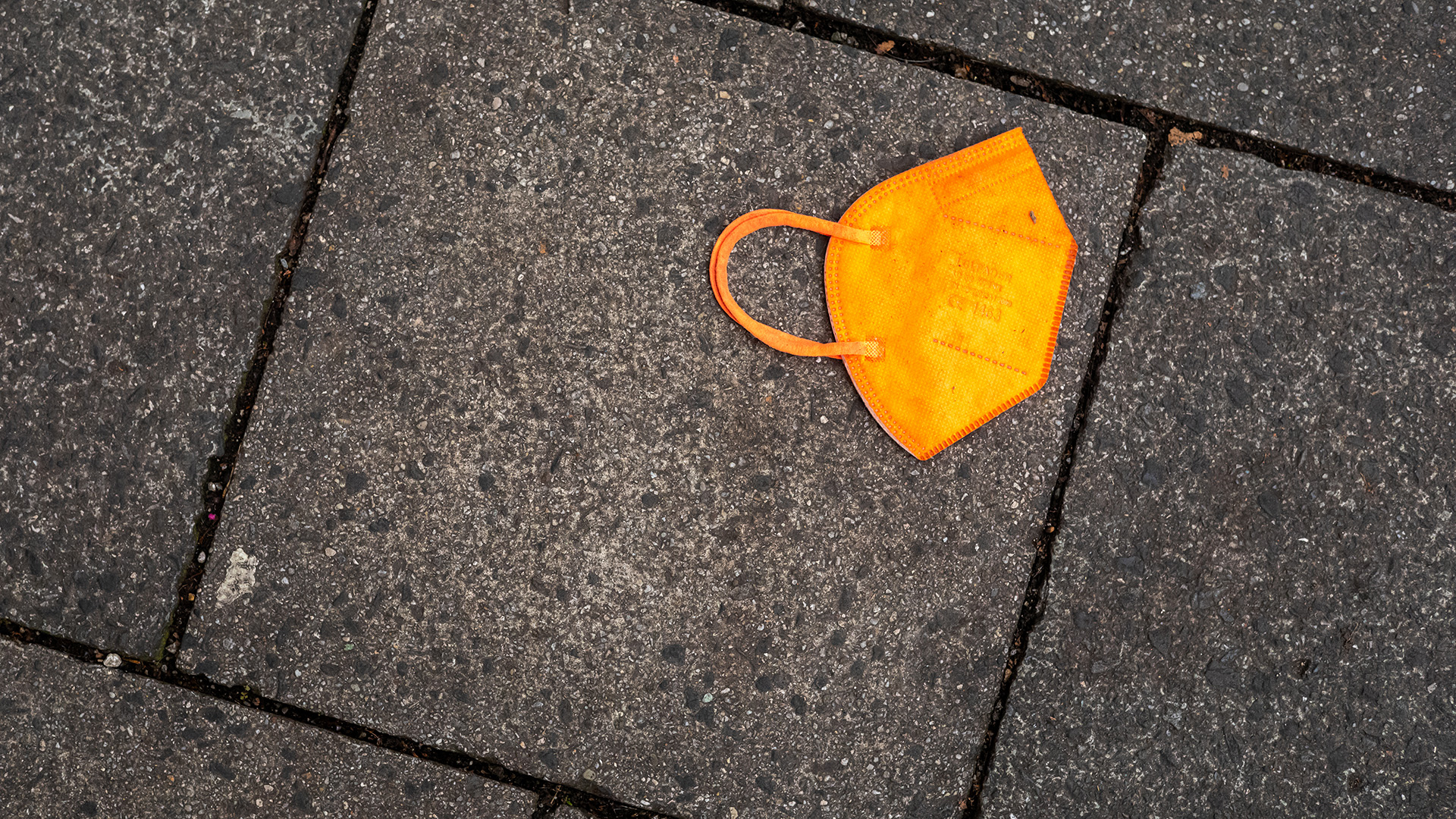 Ein gebrauchter orangefarbener Mund-Nasen-Schutz liegt auf dem Gehweg.  | picture alliance/dpa
