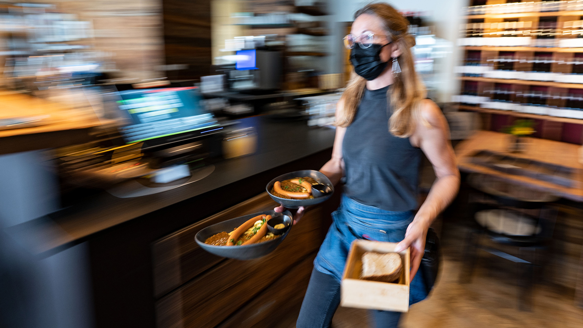  Eine Kellnerin mit Schutzmaske trägt in einem Restaurant Teller mit Essen. | dpa