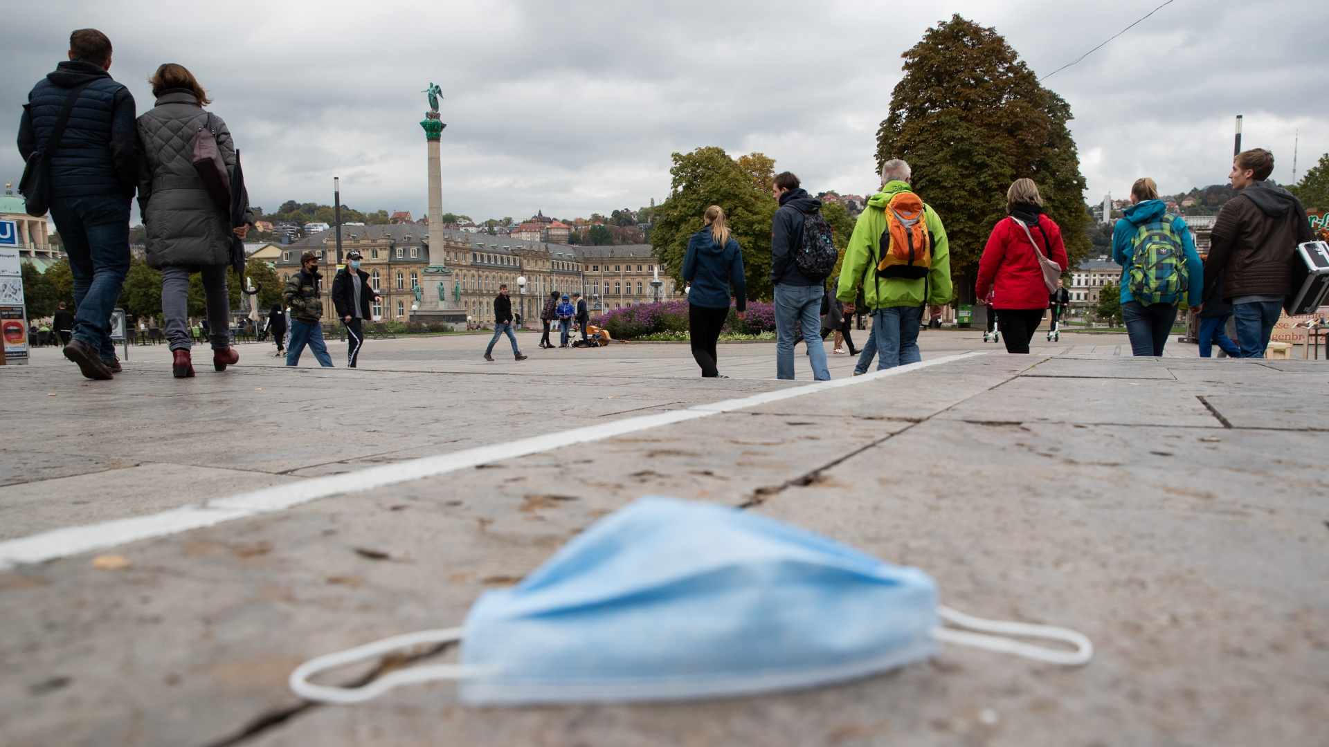 Passanten gehen über den Stuttgarter Schlossplatz, während auf dem Boden eine Mund-Nasen-Bedeckung liegt. | dpa