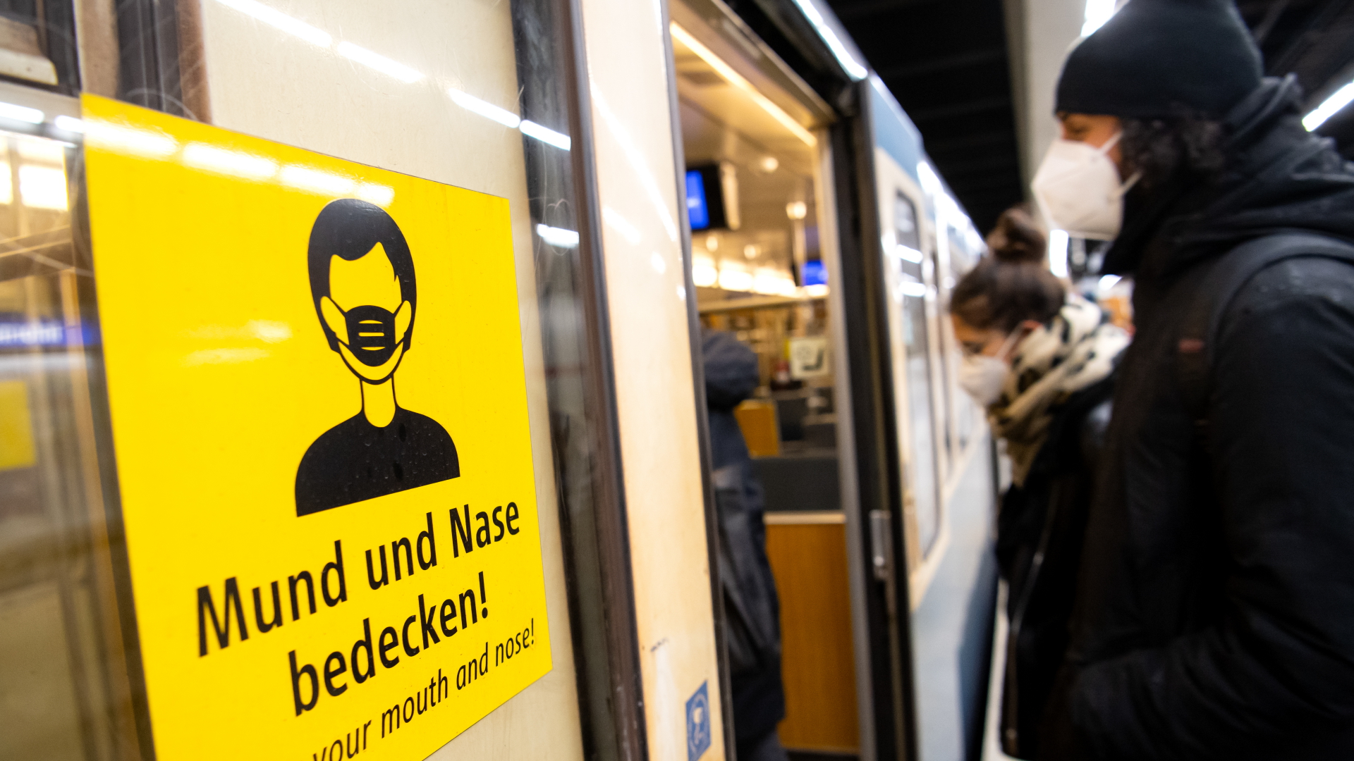 Ein Mann und eine Frau mit FFP2-Masken steigen in einer U-Bahnstation in die Bahn.