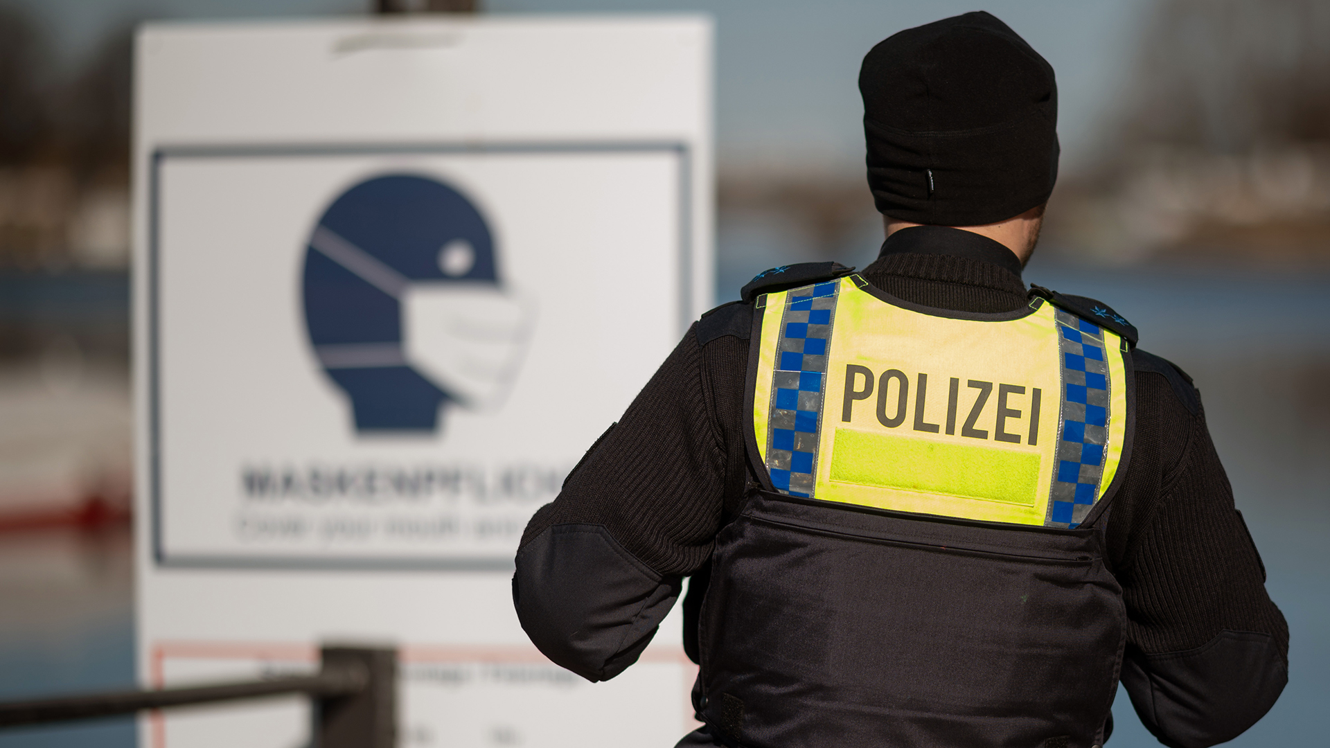 Ein Polizist steht in Hmaburg vor einem Schild mit einem Hinweis auf die Maskenpflicht. | dpa